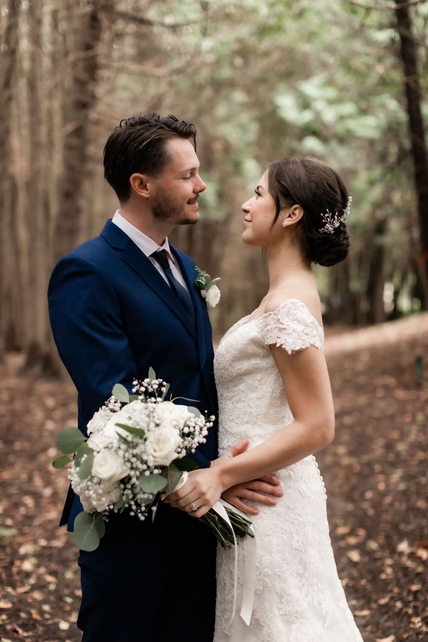 Romantic forest wedding portrait with white floral bouquet and elegant bridal attire.