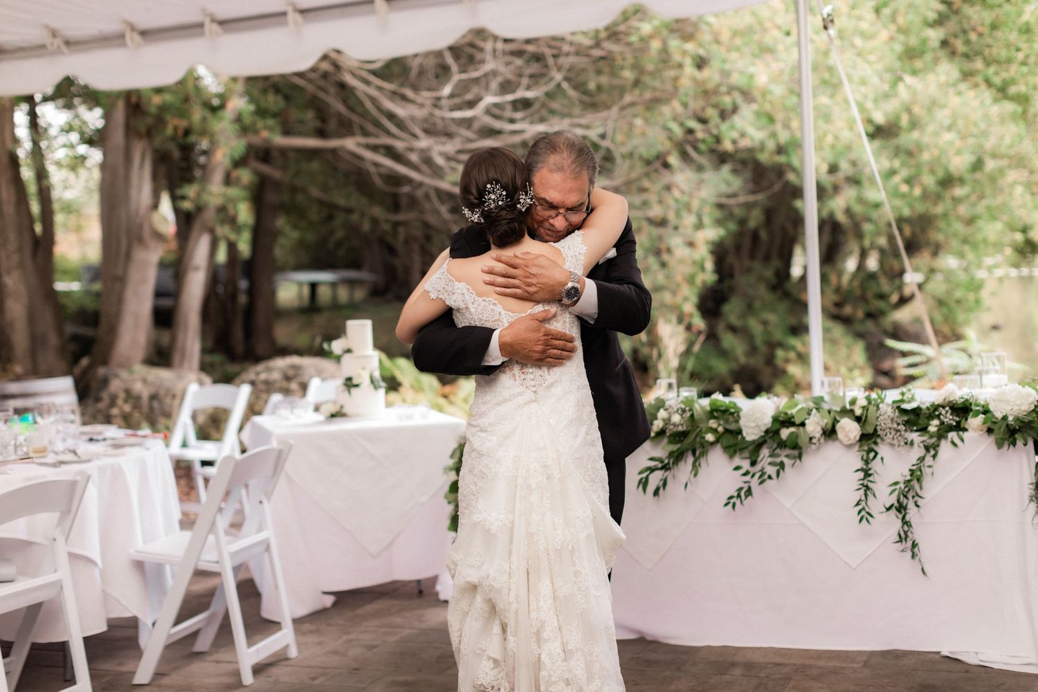 Couple embraces during their first dance at an outdoor reception under white tent.
