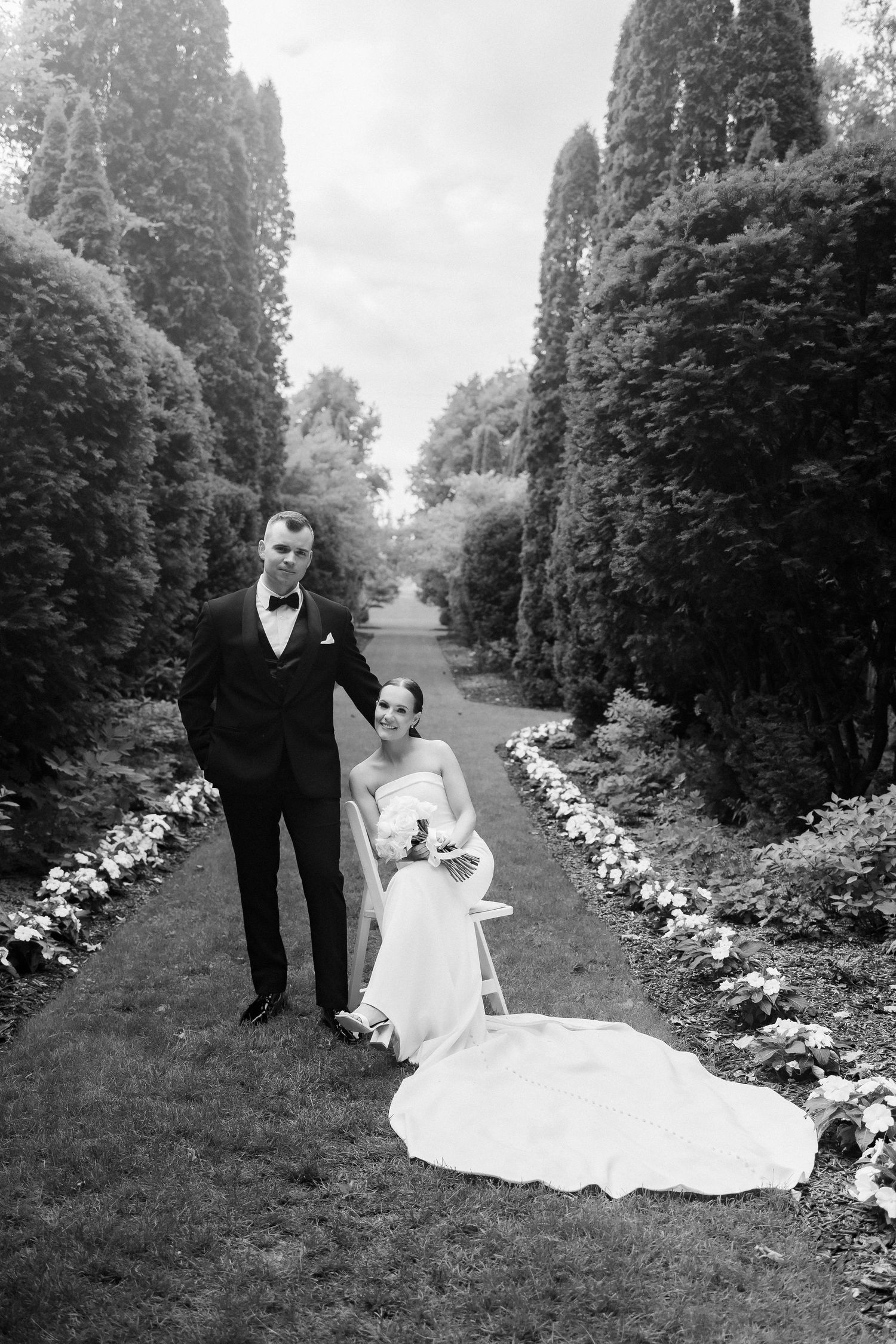 Dramatic black and white portrait of wedding couple on garden pathway with towering hedges.