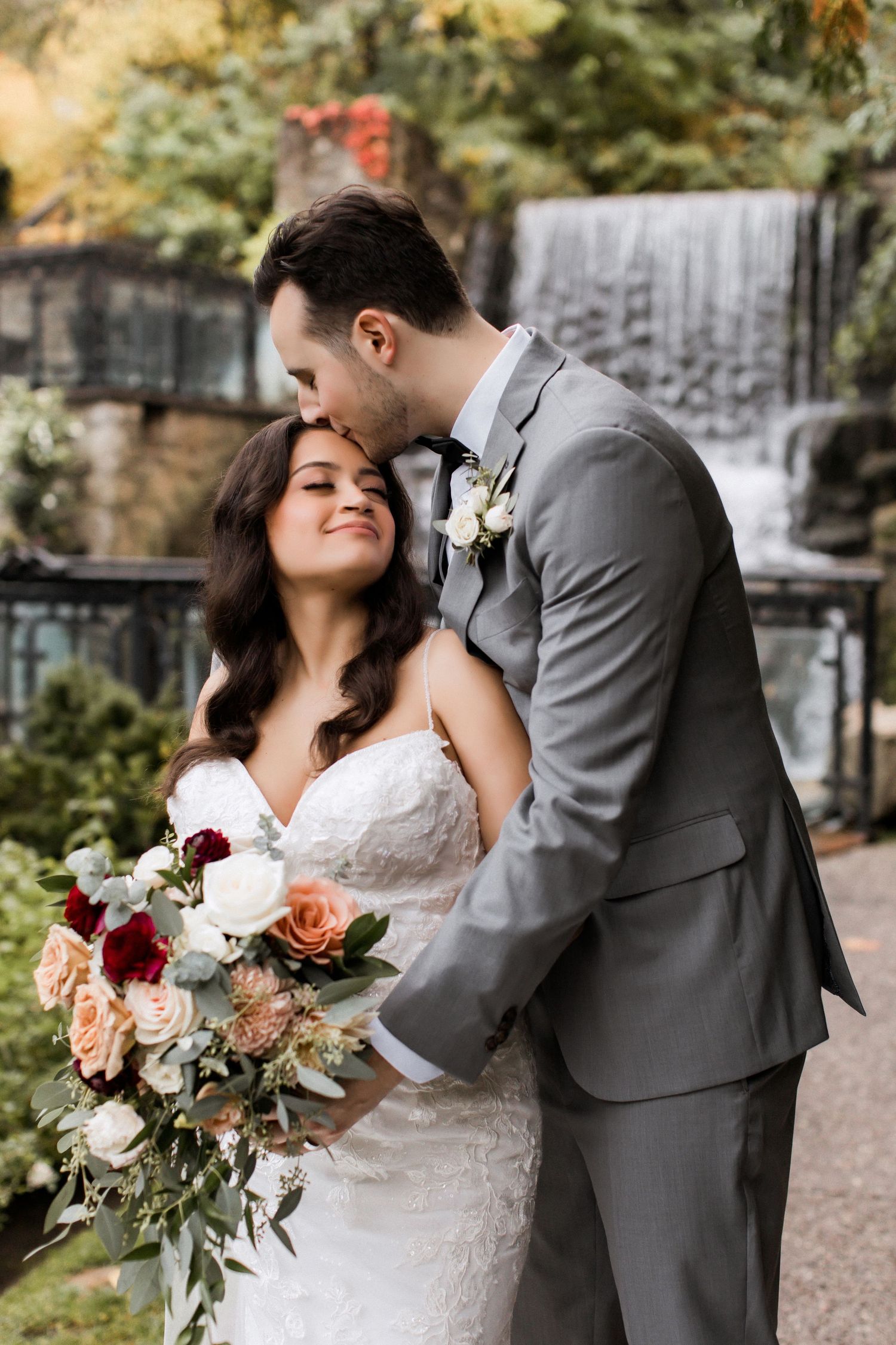 Romantic wedding moment captured with couple embracing by scenic waterfall.