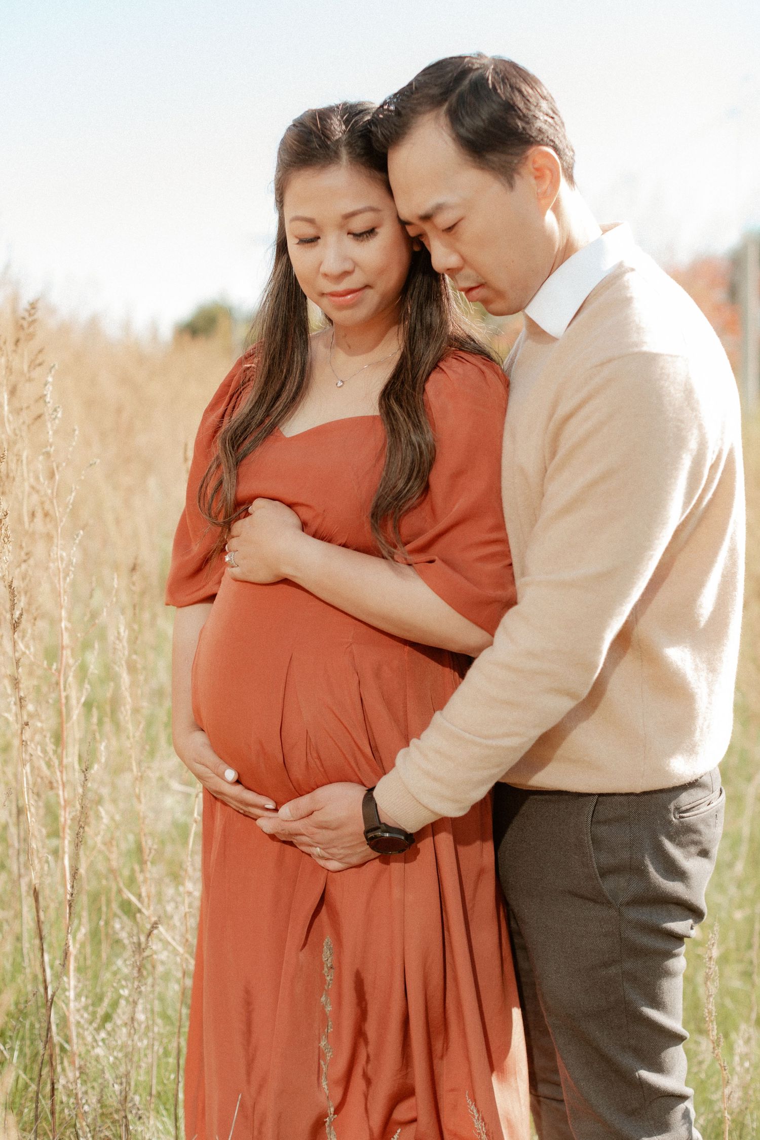 A tender maternity moment captured in warm sunlight amidst tall grass.