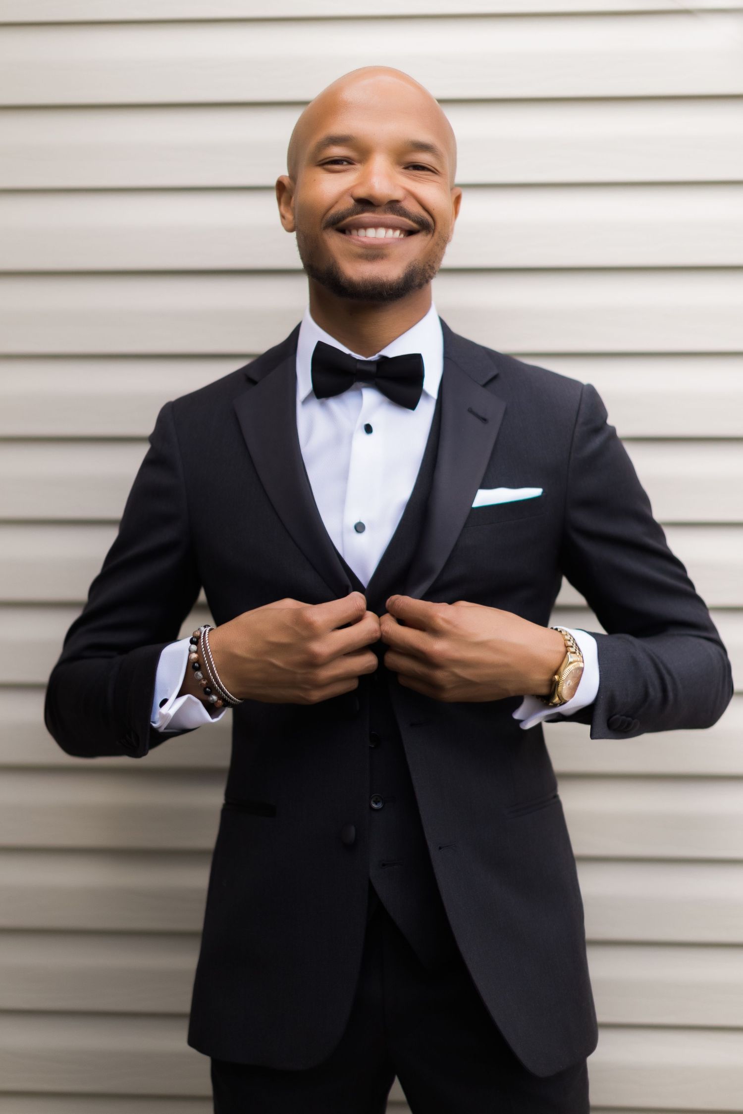 Joyful portrait of person in classic tuxedo against white siding background.
