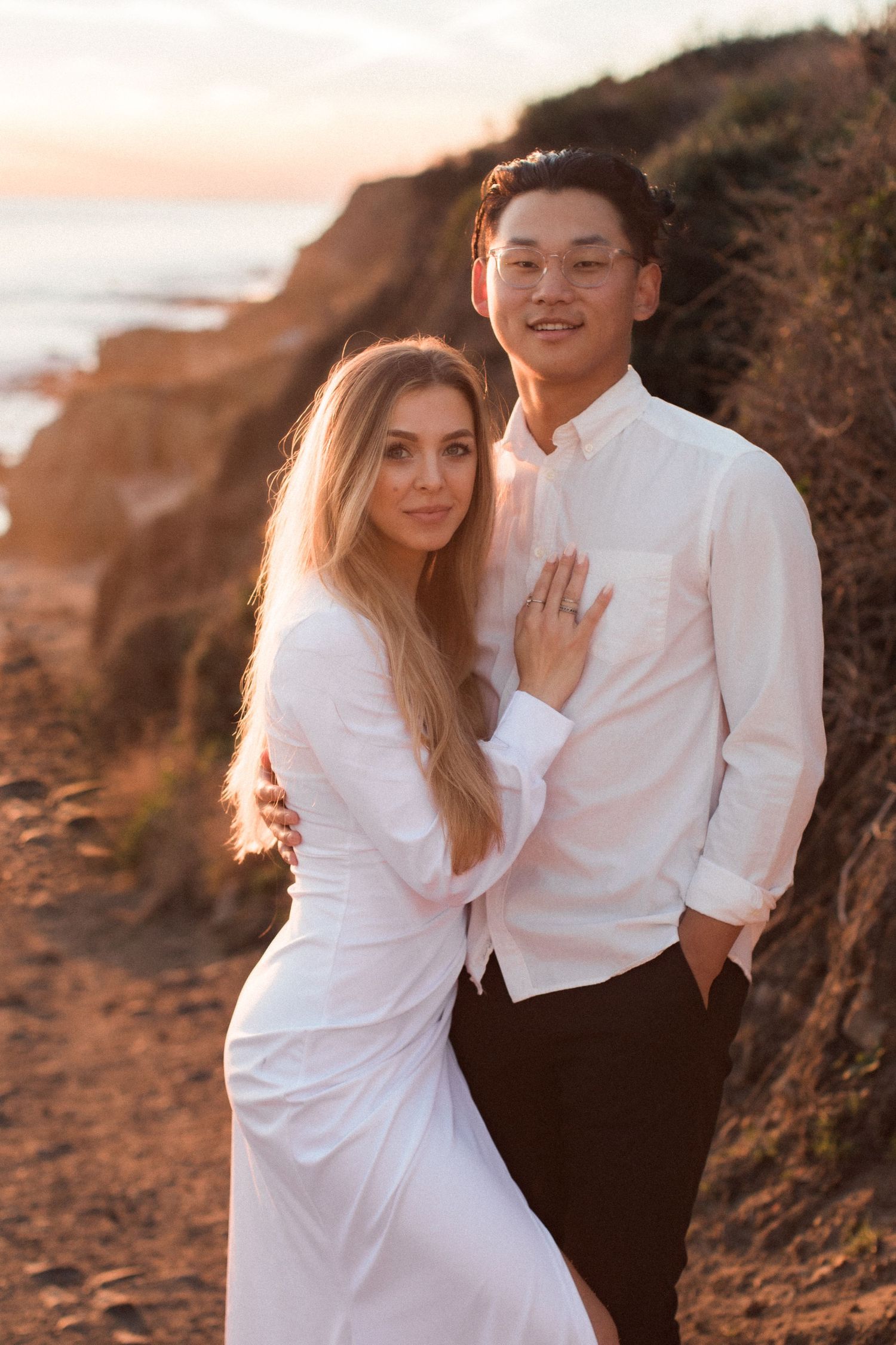 An intimate portrait of a couple in white clothing embracing on a scenic coastal cliff.