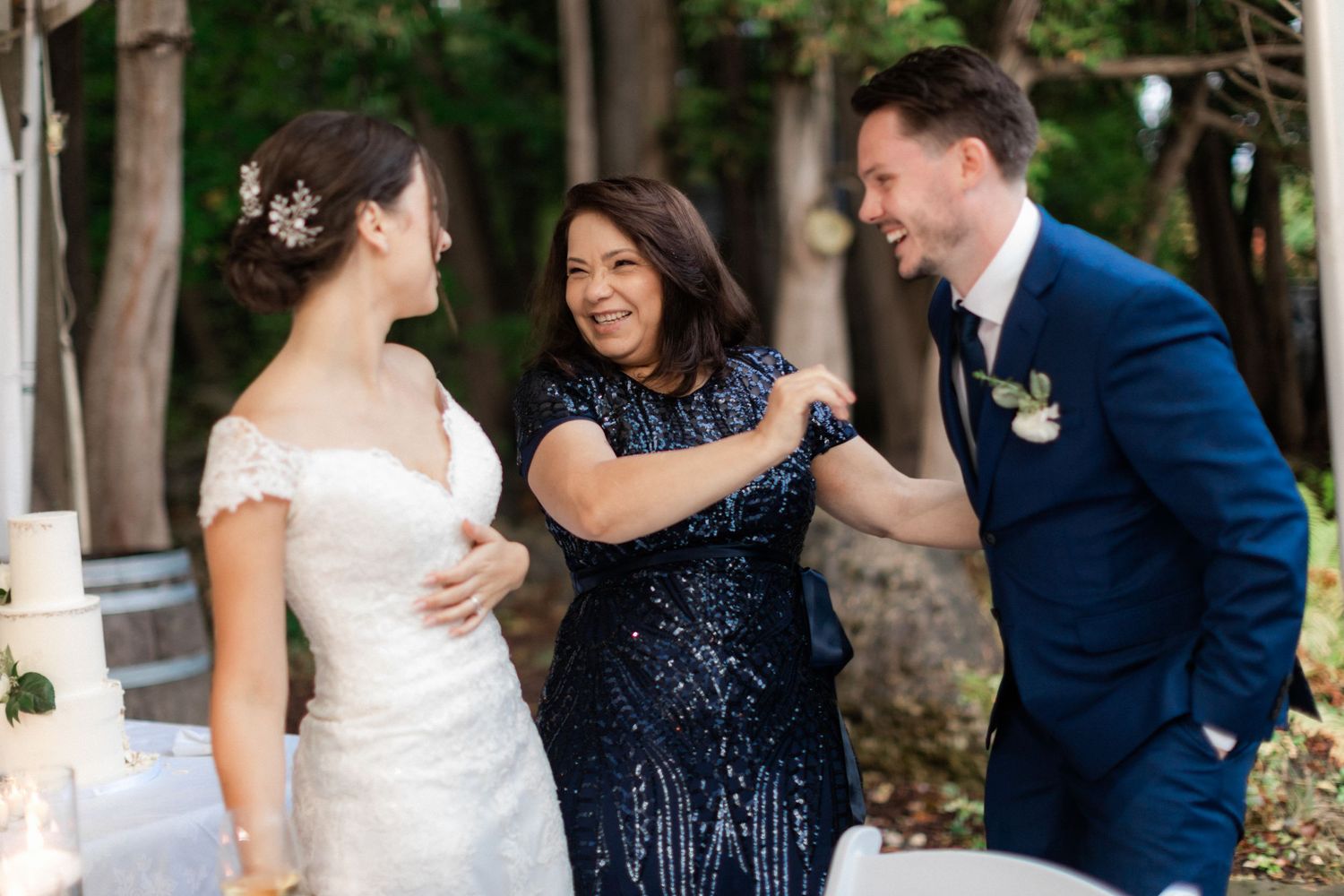 Wedding party shares a joyful moment outdoors under natural lighting with bride in white and guest in navy sequins.