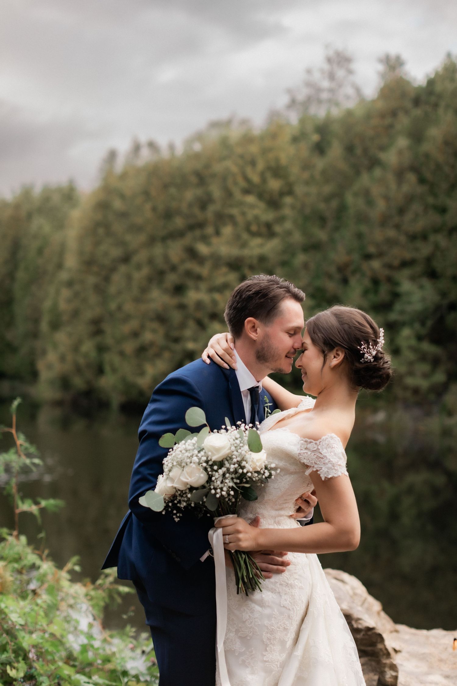 A romantic wedding portrait by a lake with the couple embracing among nature.
