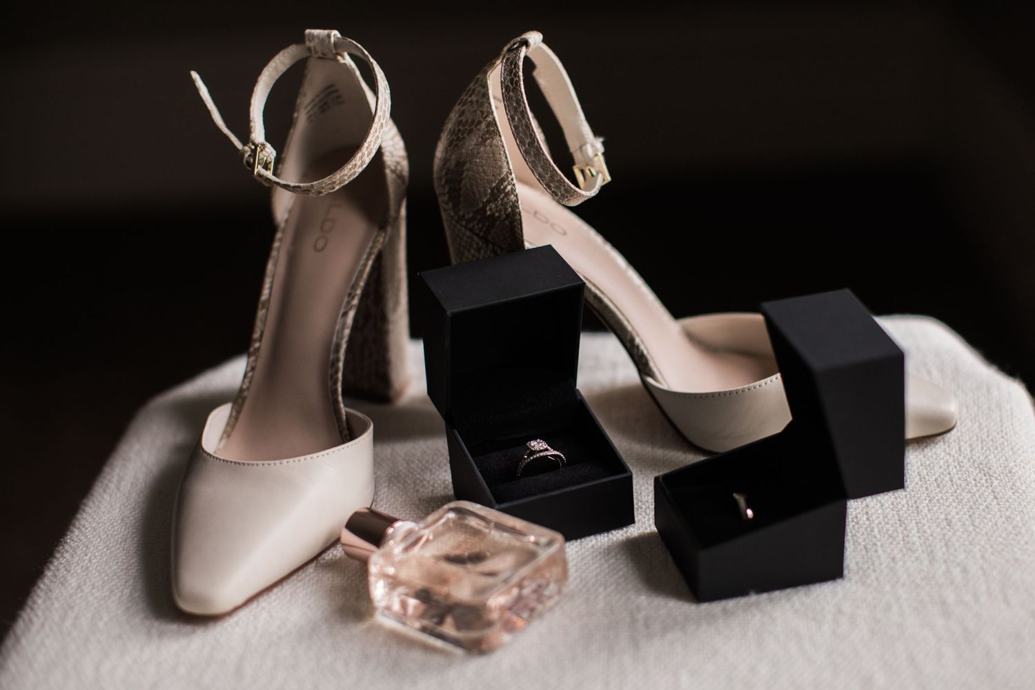 Wedding accessories including cream heels, jewelry box and perfume bottle on white surface.