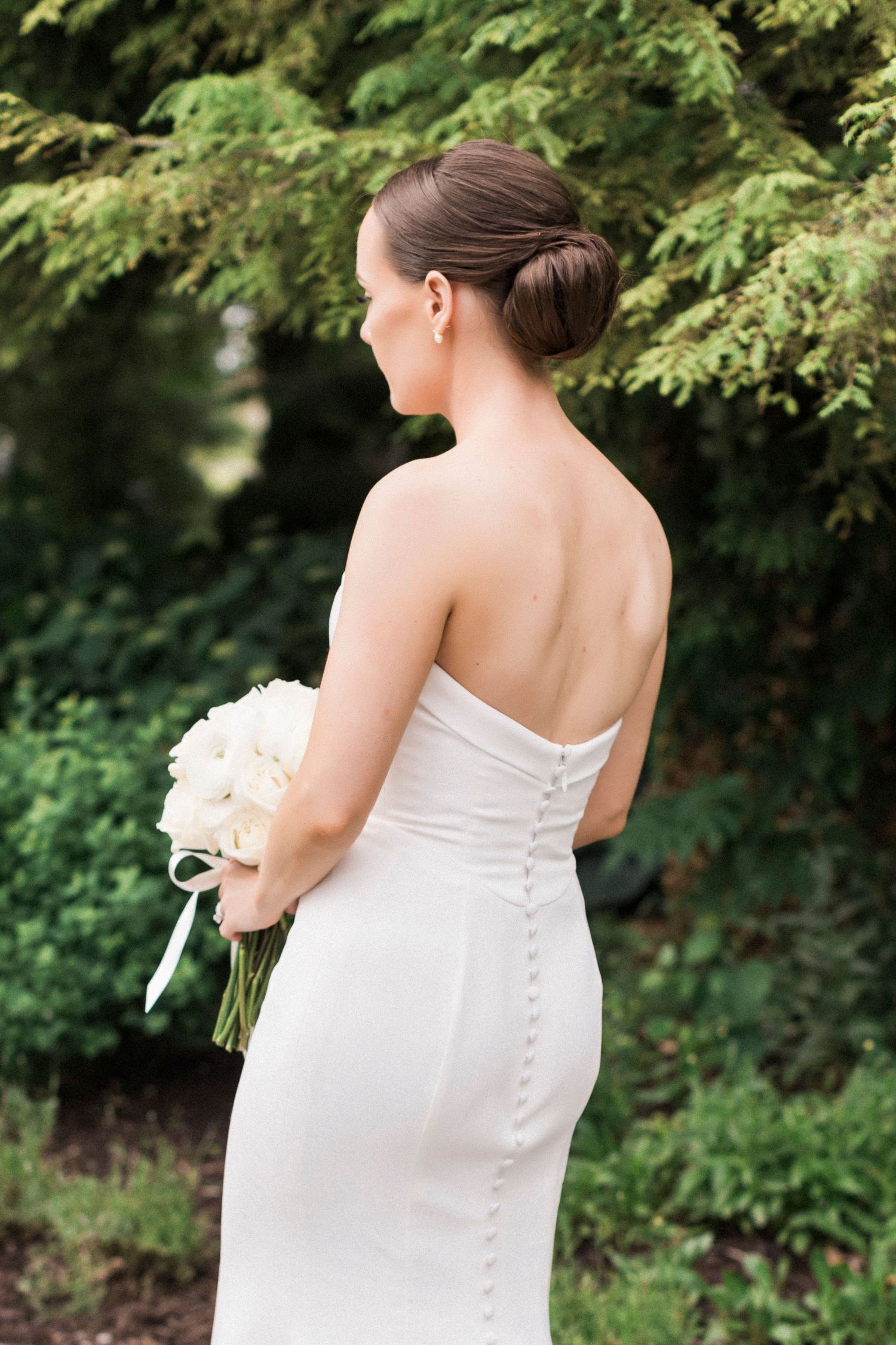 Elegant bridal back detail showing white dress with button closure and bouquet.