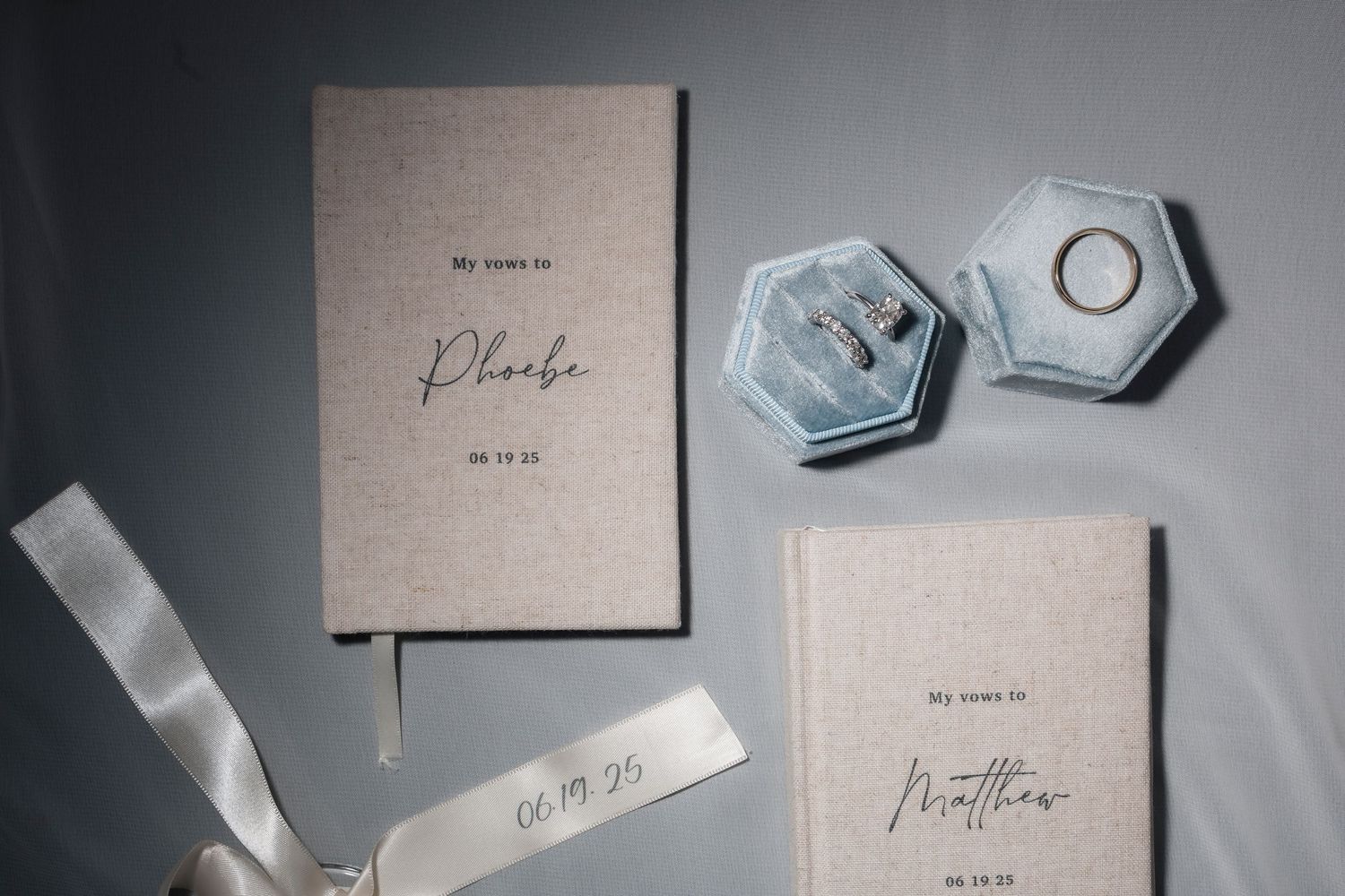 Wedding vow books and hexagonal ring boxes arranged on a gray surface with soft, elegant styling.