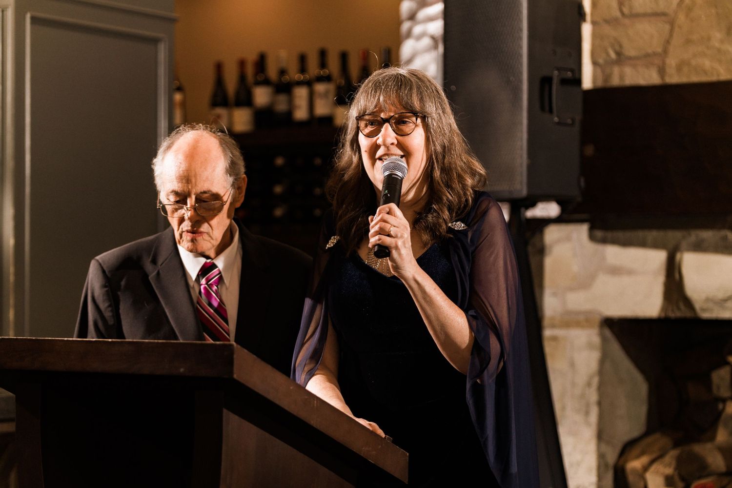 Speakers delivering wedding toasts at rustic venue with stone walls.