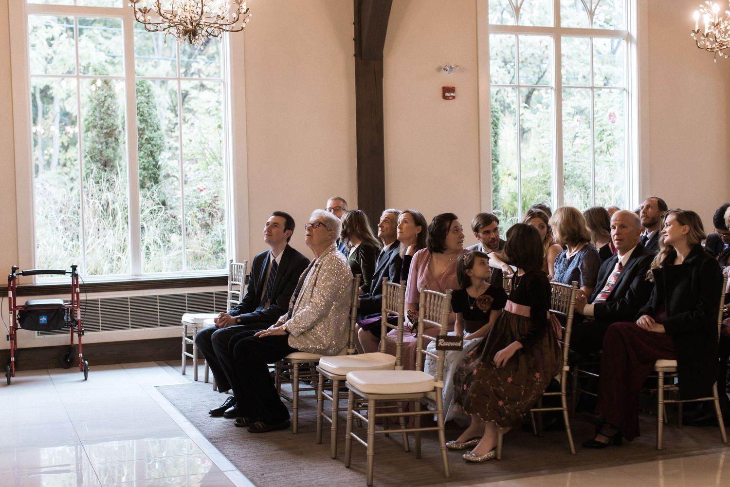 Wedding ceremony guests seated in elegant chapel with natural light streaming through windows.