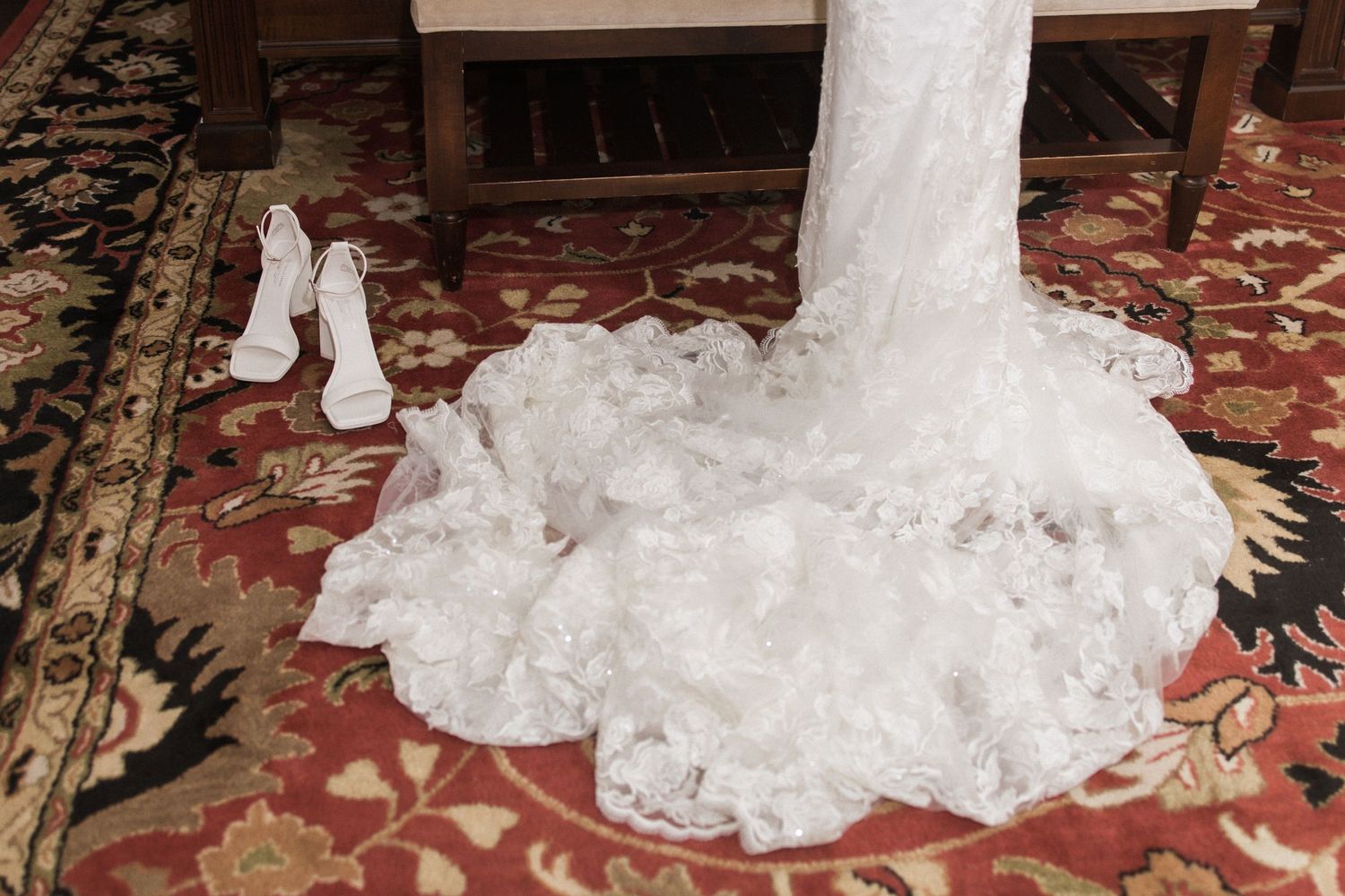 White wedding dress and shoes displayed on ornate red and gold carpet.