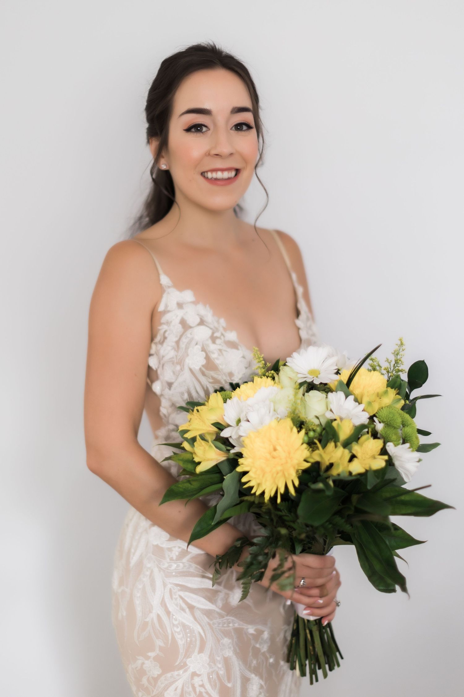 Woman in white lace wedding dress holds yellow and white floral bouquet.