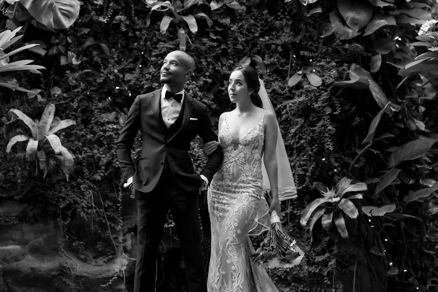 Black and white wedding photo of a couple standing in front of a garden wall backdrop.