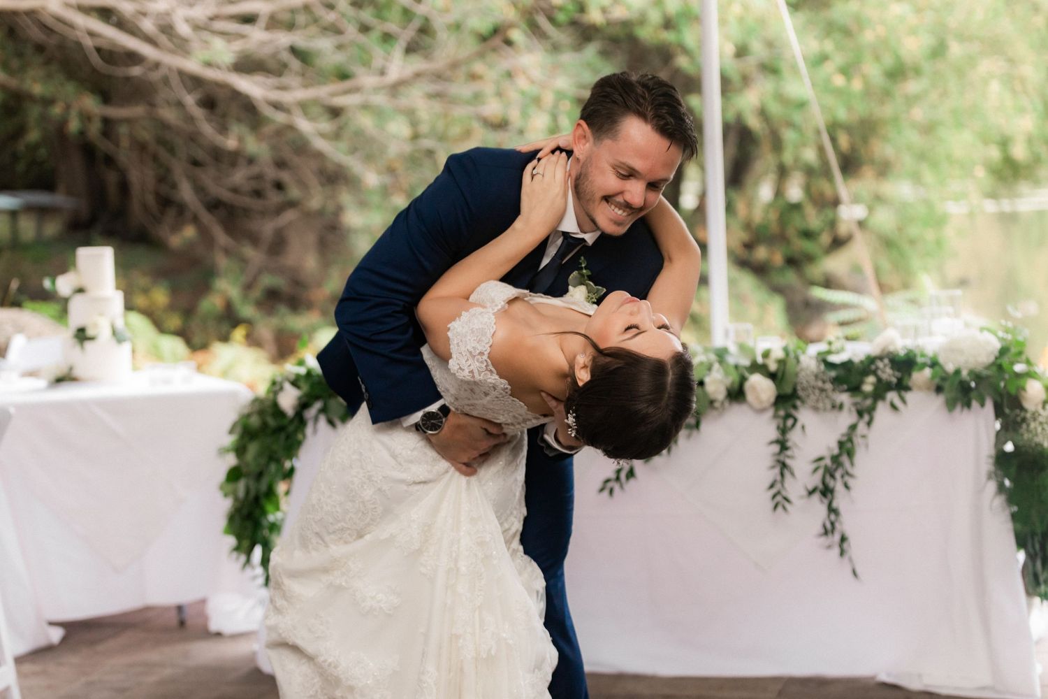 A romantic dip during the wedding reception with white decor and natural greenery in background.