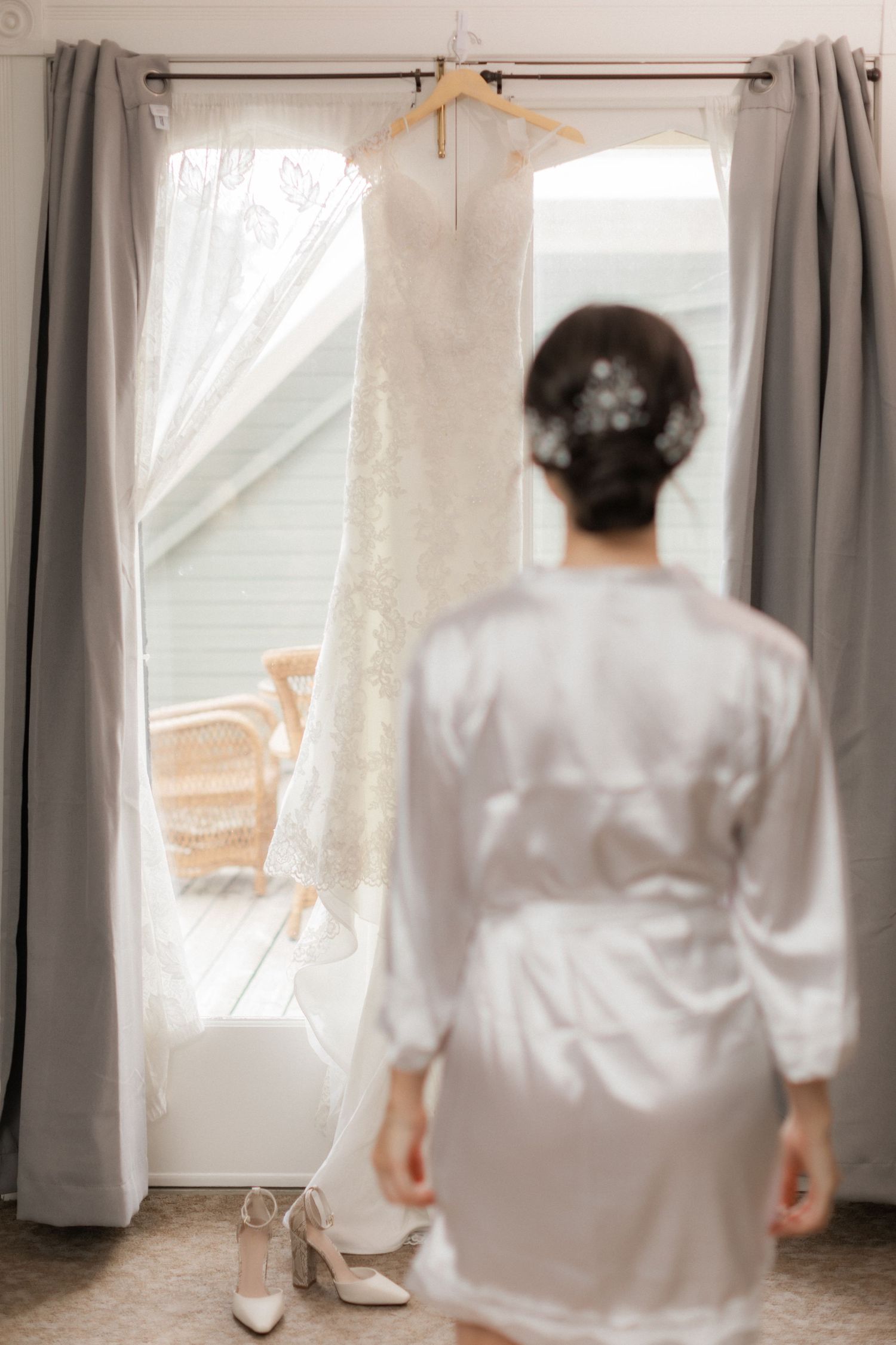 White lace wedding dress hangs by window with silhouette in foreground.