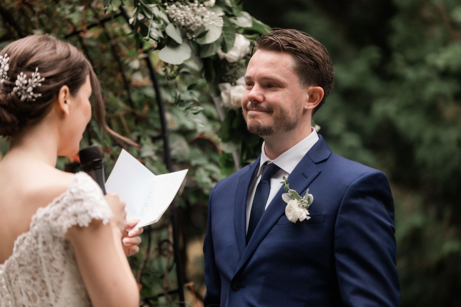 A couple exchanges vows during an outdoor garden wedding ceremony under floral arrangements.