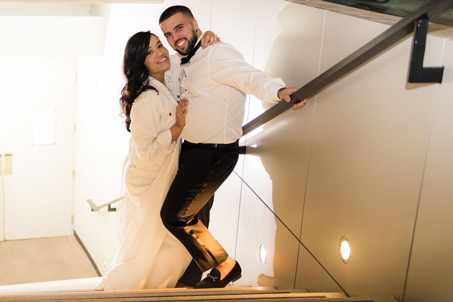 A couple dances joyfully on a staircase at their wedding reception.