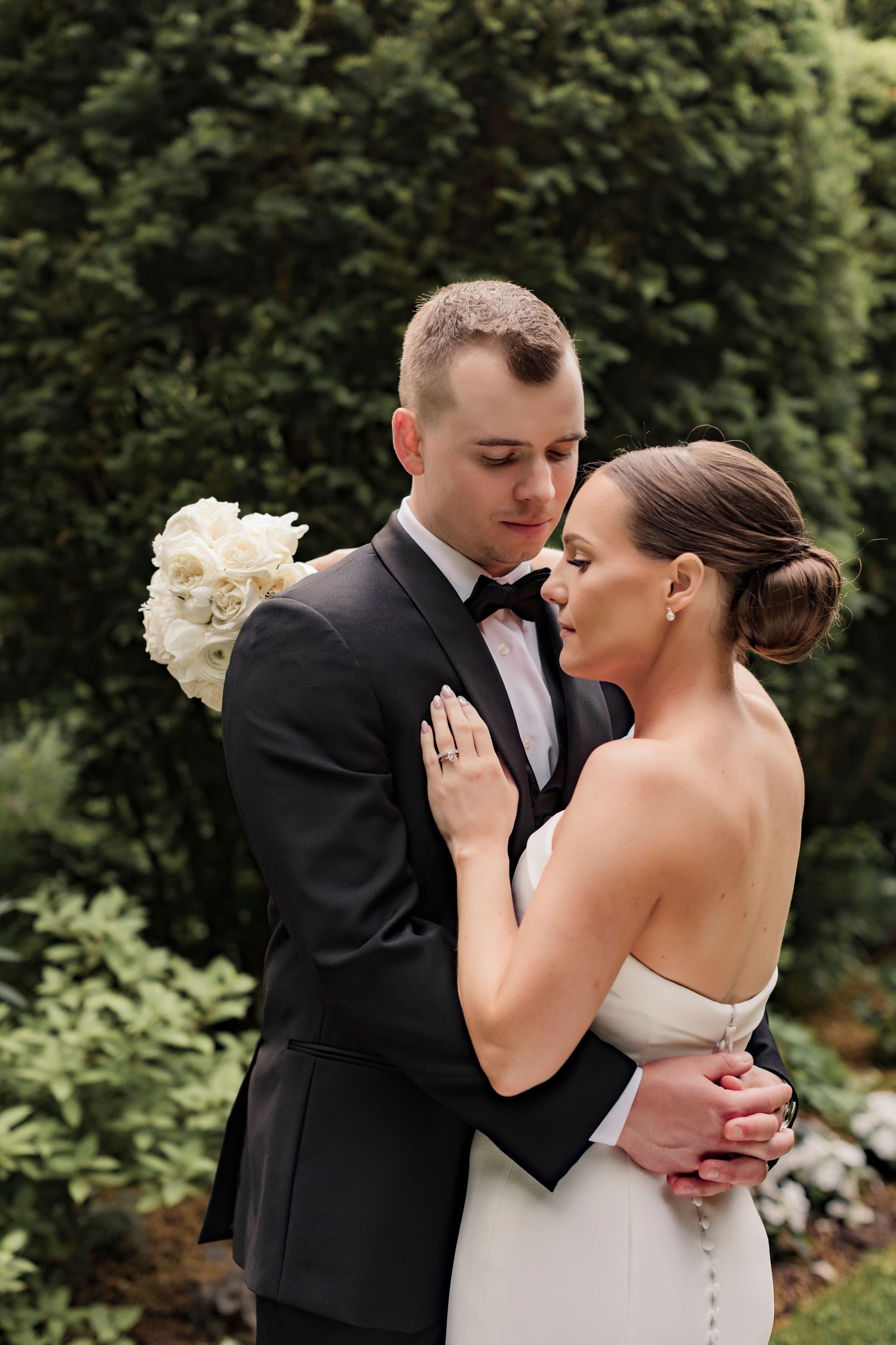 Intimate wedding portrait of a couple embracing outdoors with white flowers and greenery.