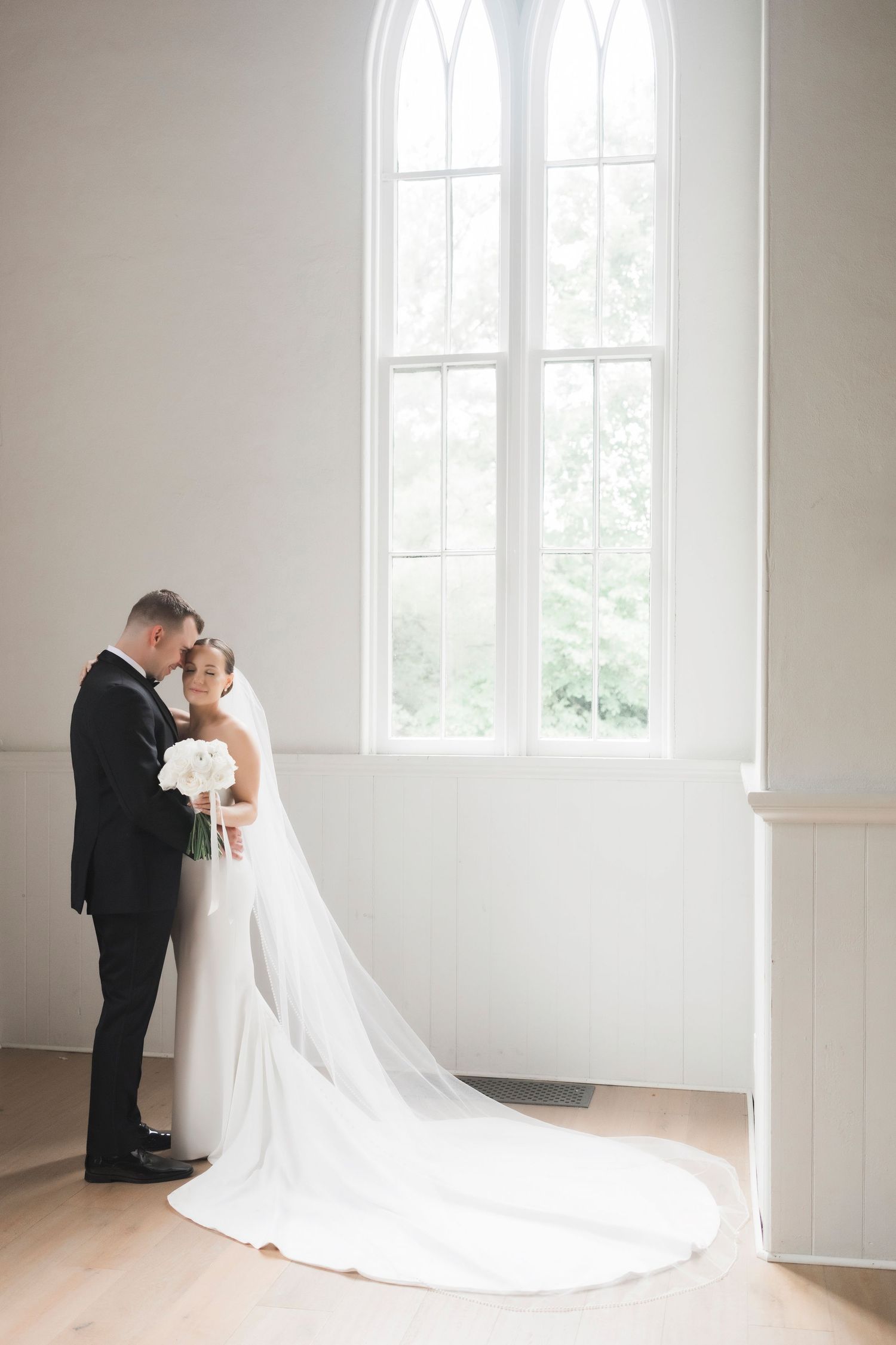 A classic minimalist wedding photoshoot in a bright white room with tall windows.