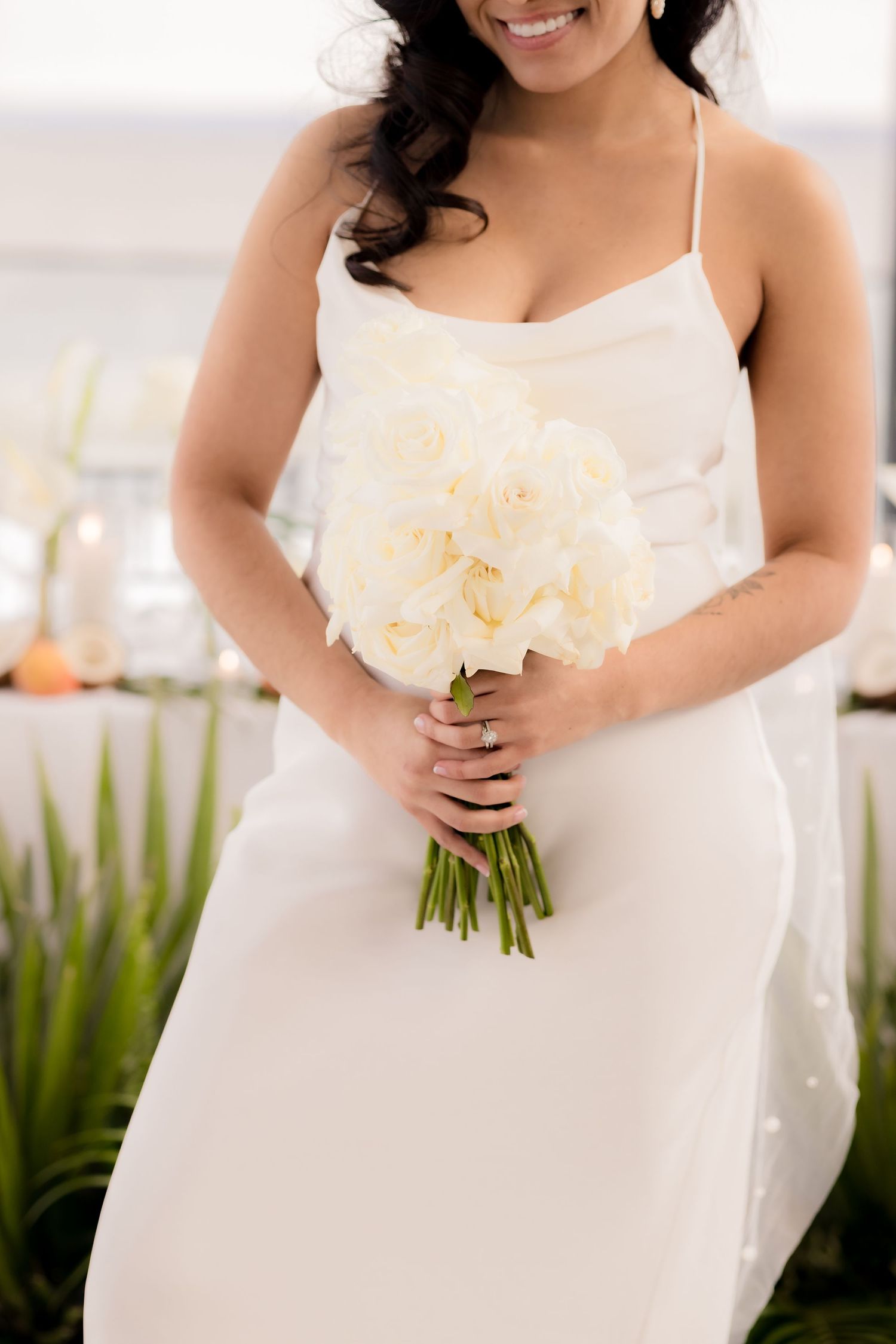 Bride in simple white dress holding cream-colored bouquet against modern decor.