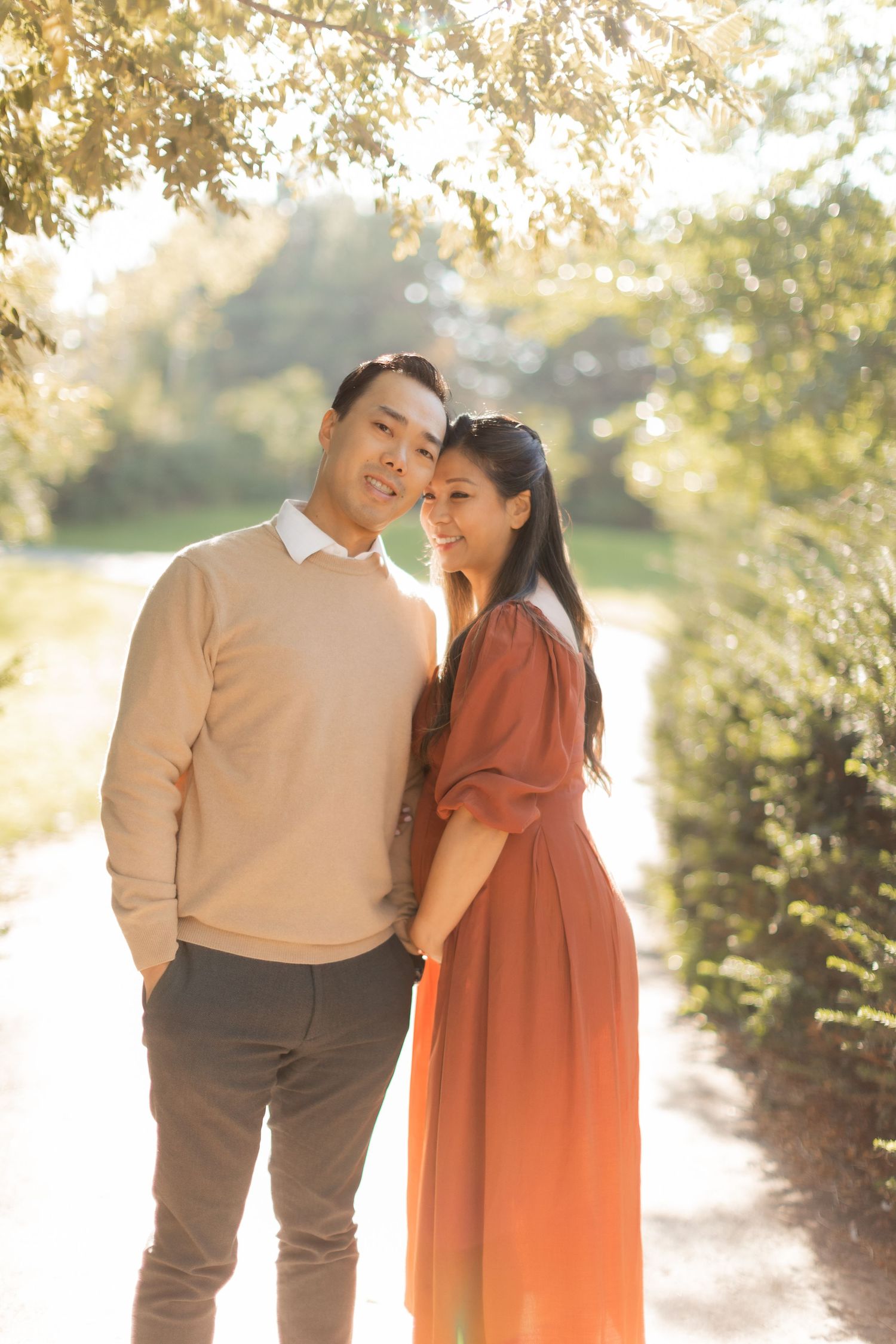 Intimate pregnancy portrait of couple embracing on garden path in warm afternoon light.