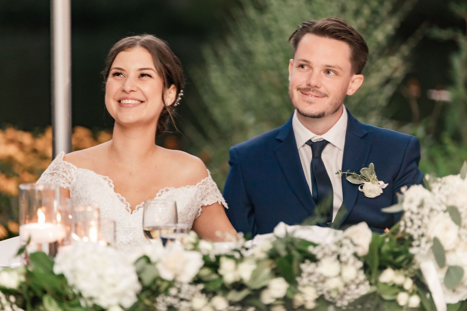 Couple shares candid moment at reception table decorated with white floral centerpieces.