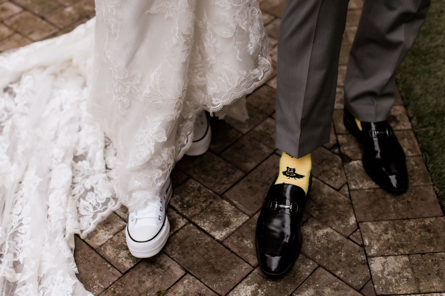 Contrasting footwear of bride in sneakers and groom in formal shoes on stone pavers.