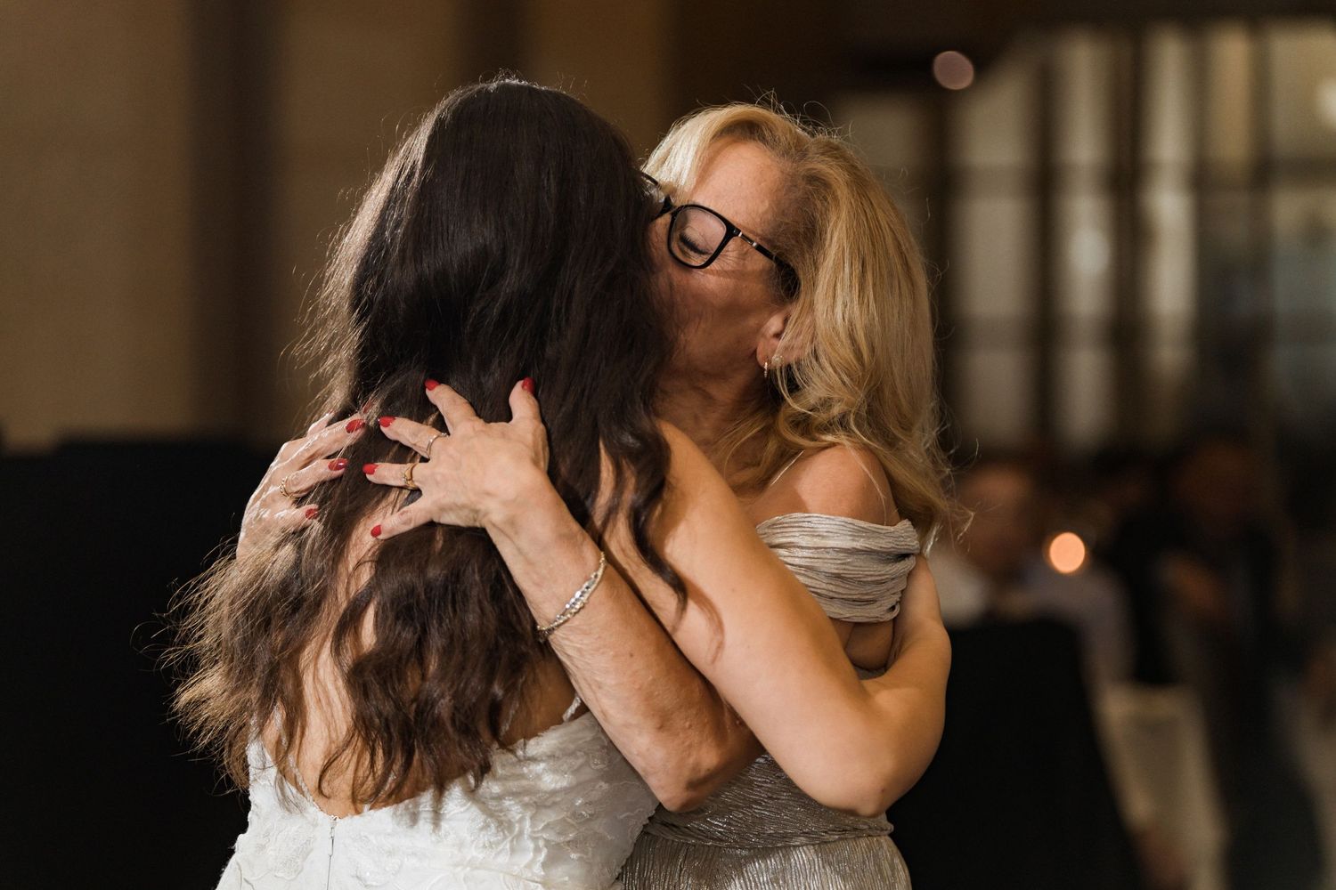 Friends share an emotional embrace while wearing matching white formal dresses.