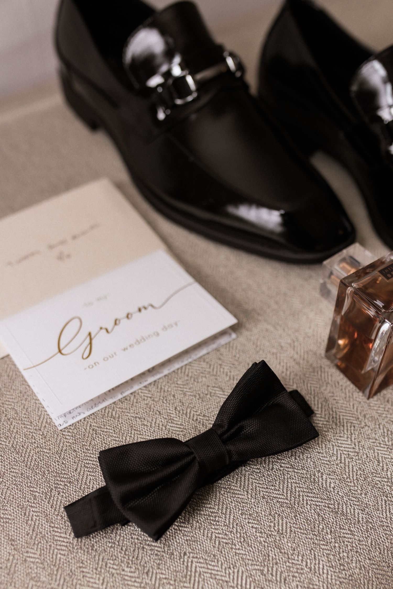 Black patent leather dress shoes with bow tie and handwritten note on textured fabric.