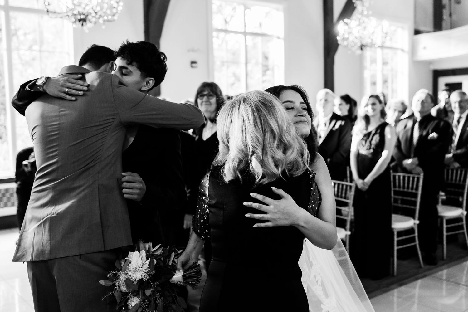 Black and white photo capturing emotional group hug during wedding celebration.