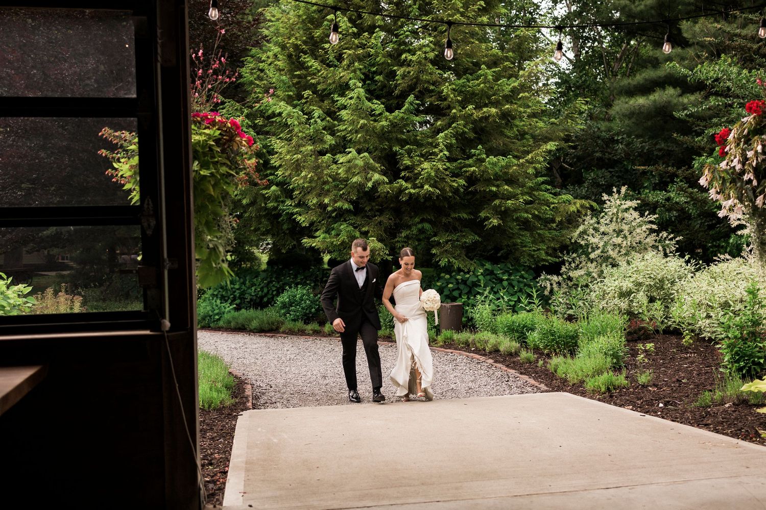 Couple walking together down a winding garden path surrounded by lush greenery and summer blooms in an outdoor setting.
