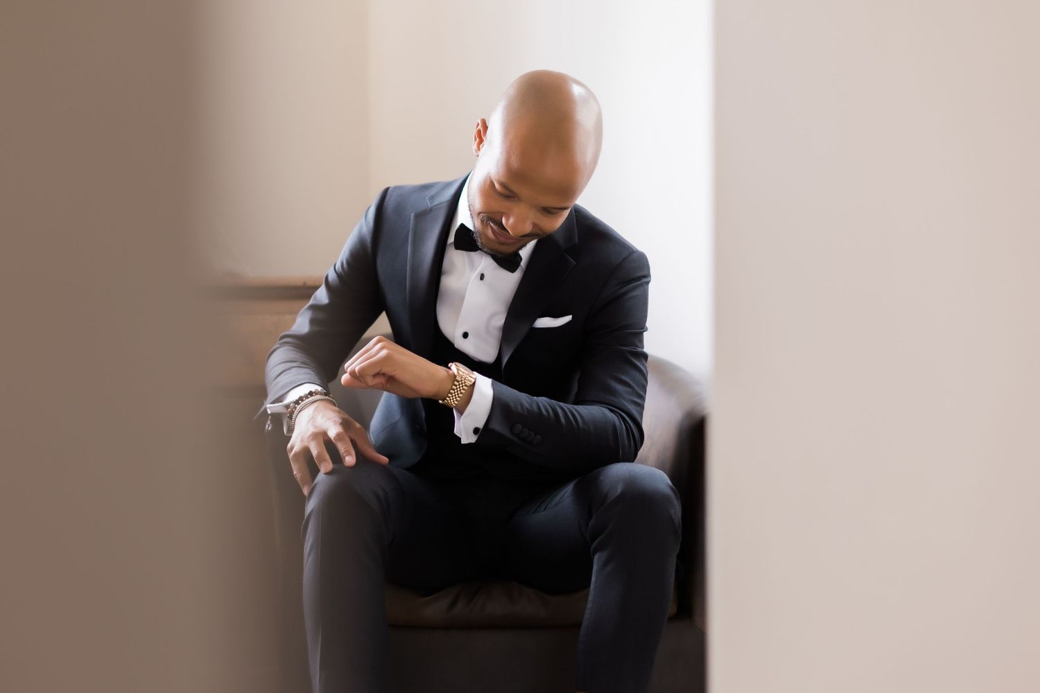 Well-dressed person in tuxedo checks time while seated in leather chair.