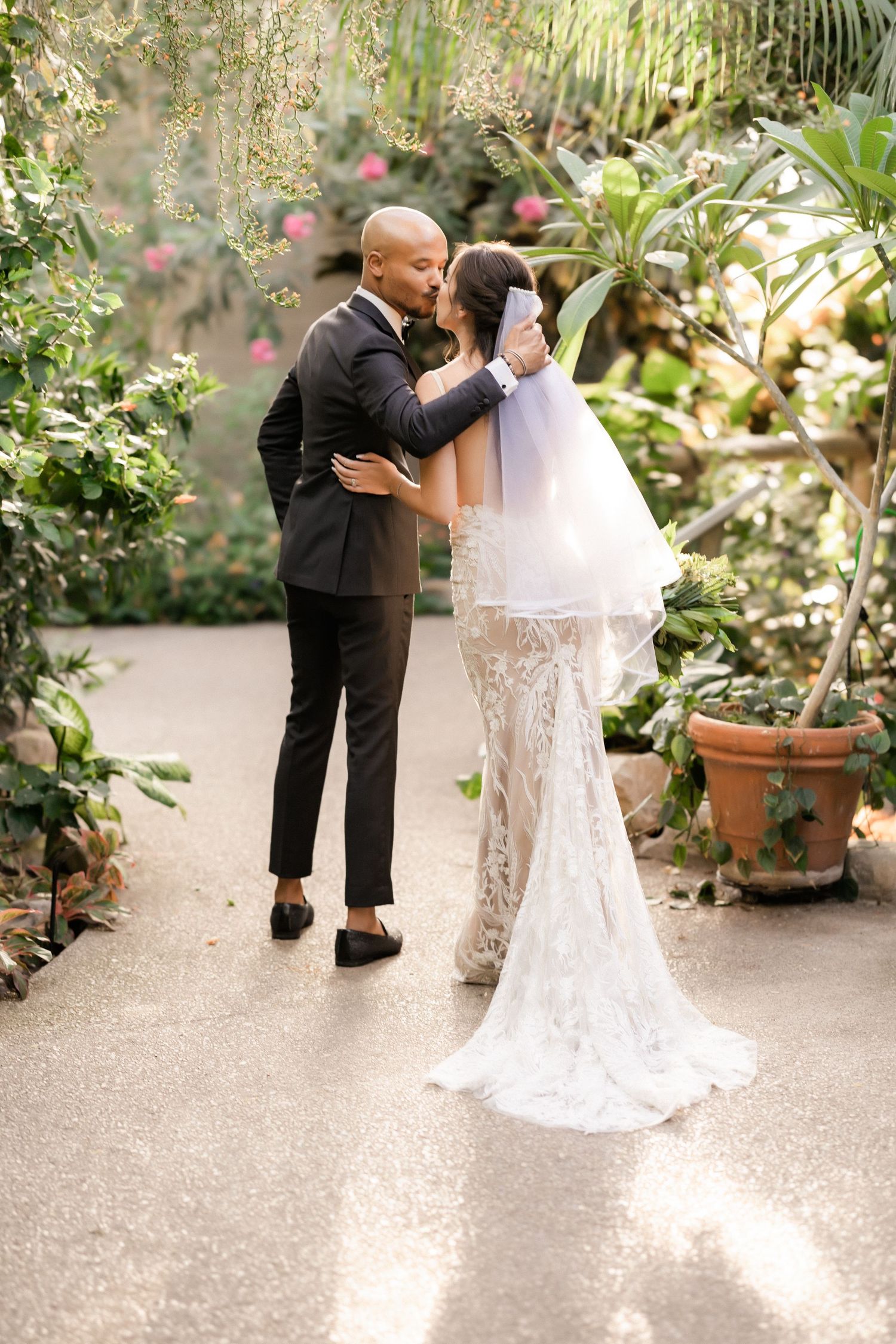 A romantic moment between newlyweds in an elegant garden setting with potted plants.