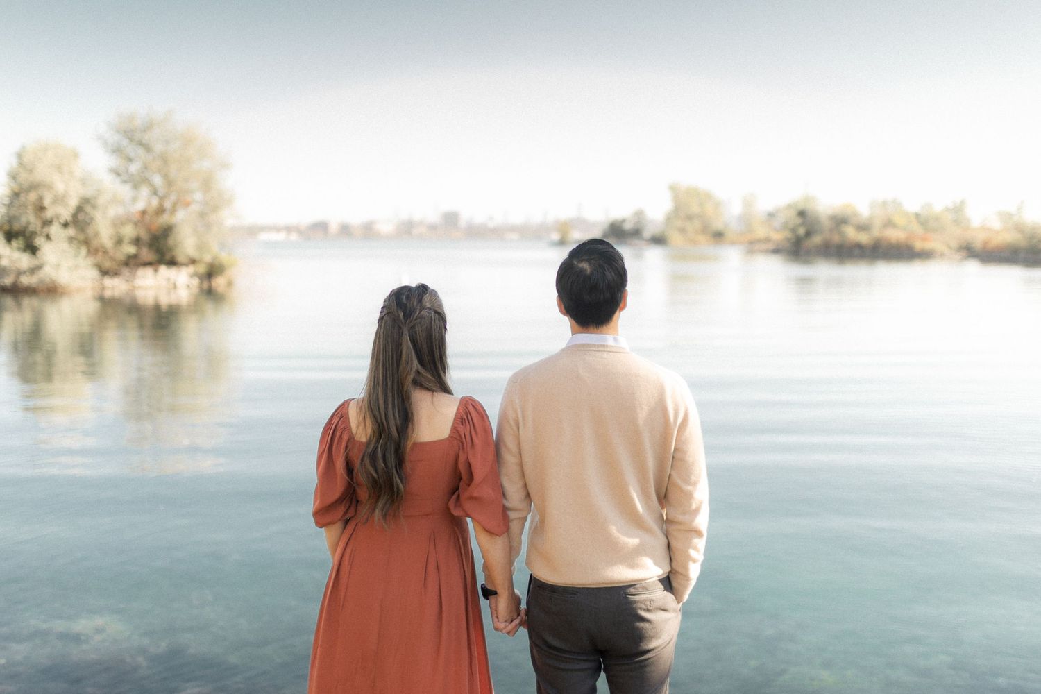 Couple gazes at lake view during maternity photoshoot in complementary outfits.
