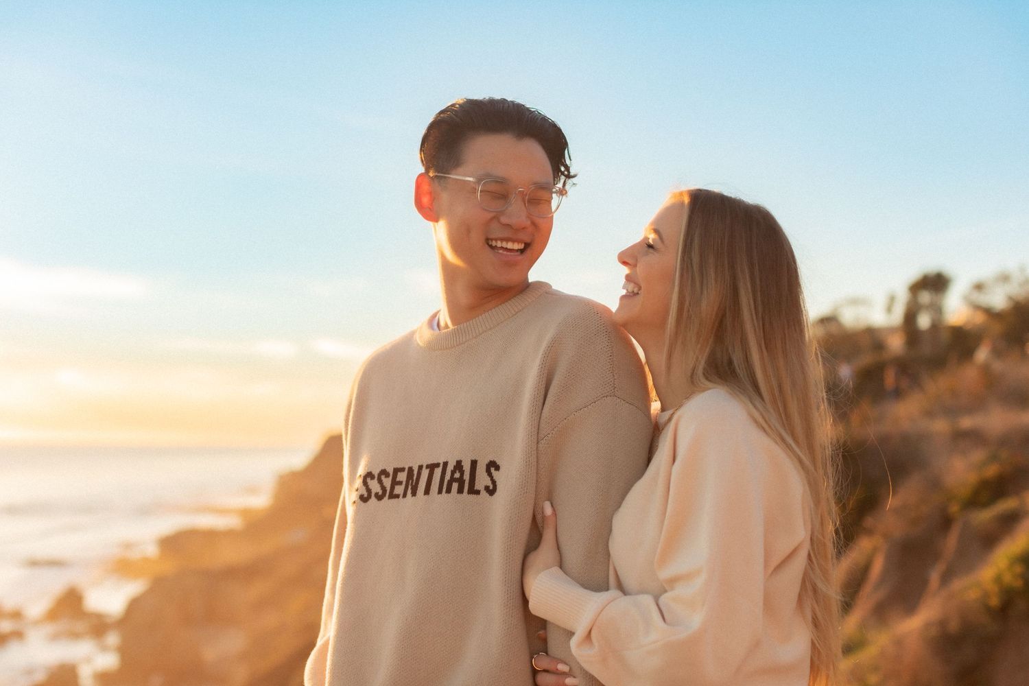 A joyful moment shared between a couple on a scenic cliff overlooking the ocean at golden hour.