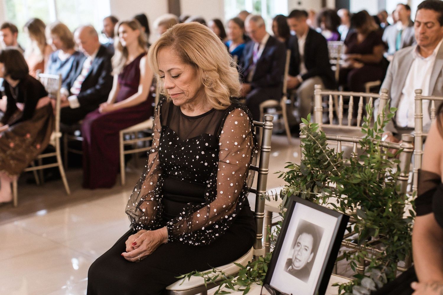 Guest in sparkly black dress seated next to framed photo during wedding ceremony.