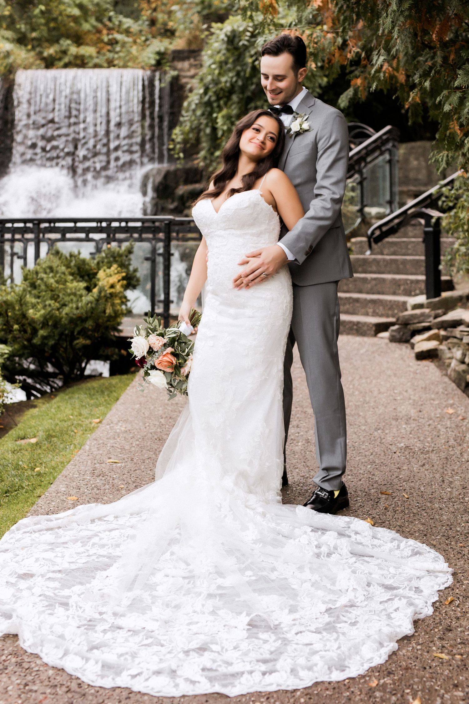 Newlyweds pose by cascading waterfall with bride's stunning lace train on display.
