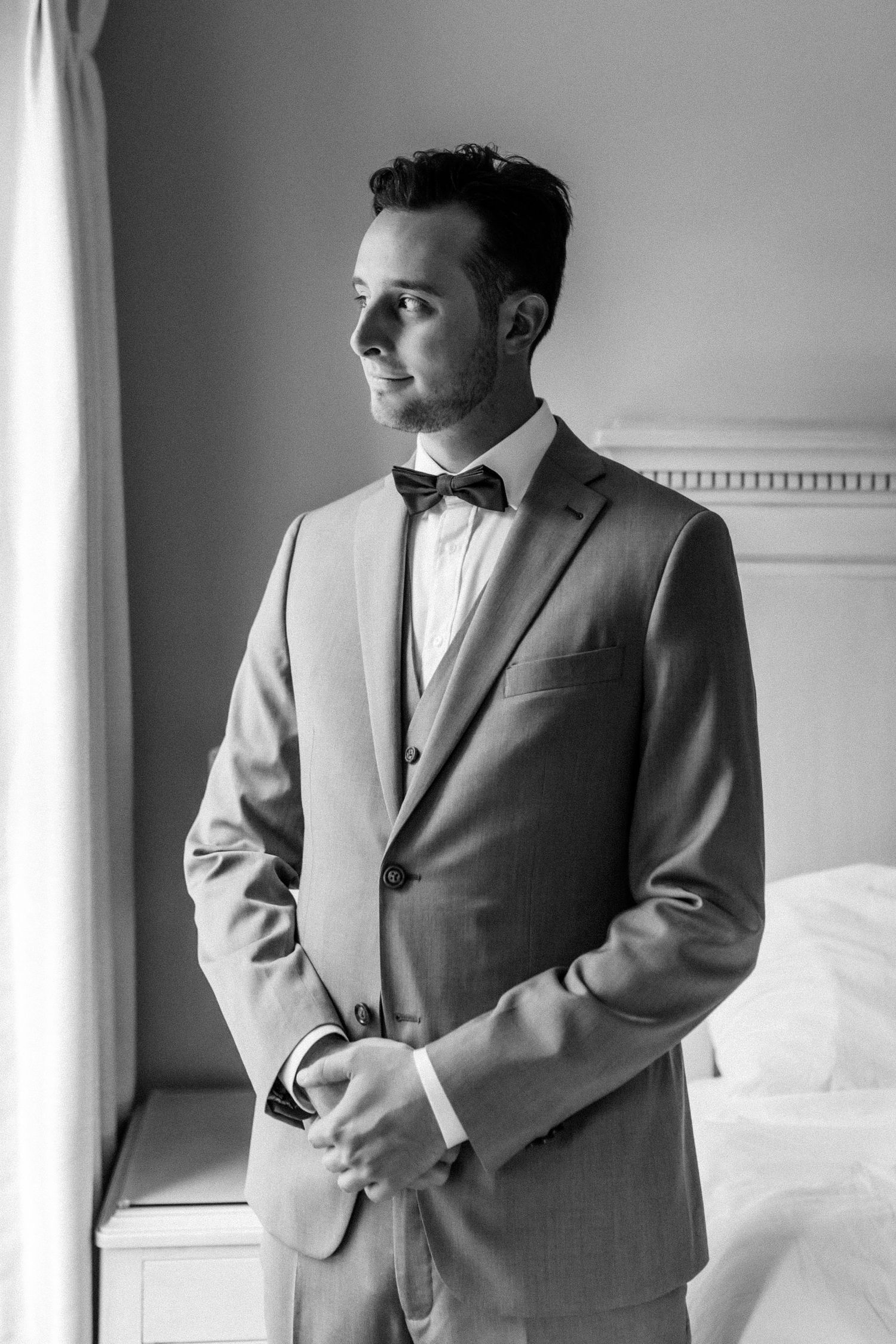 Classic black and white portrait of groom in formal grey suit by window.