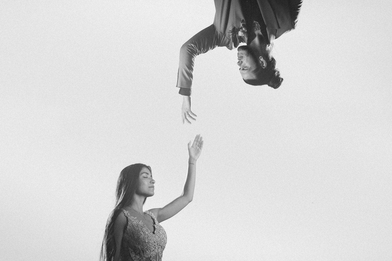 Artistic black and white photo of two people reaching toward each other against a bright sky.