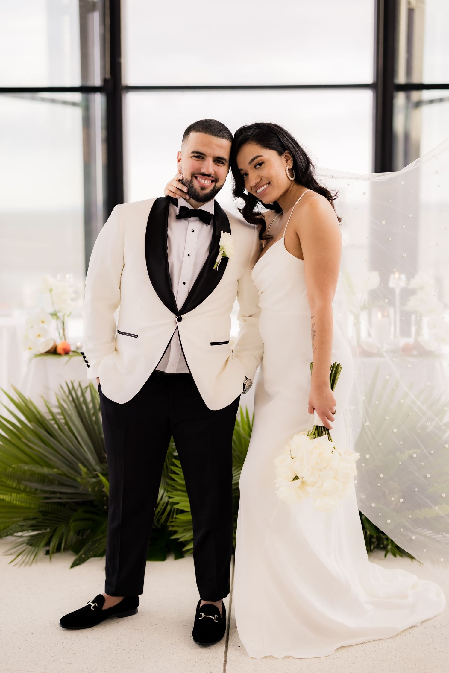 Happy newlyweds embrace during wedding portraits in modern white venue.