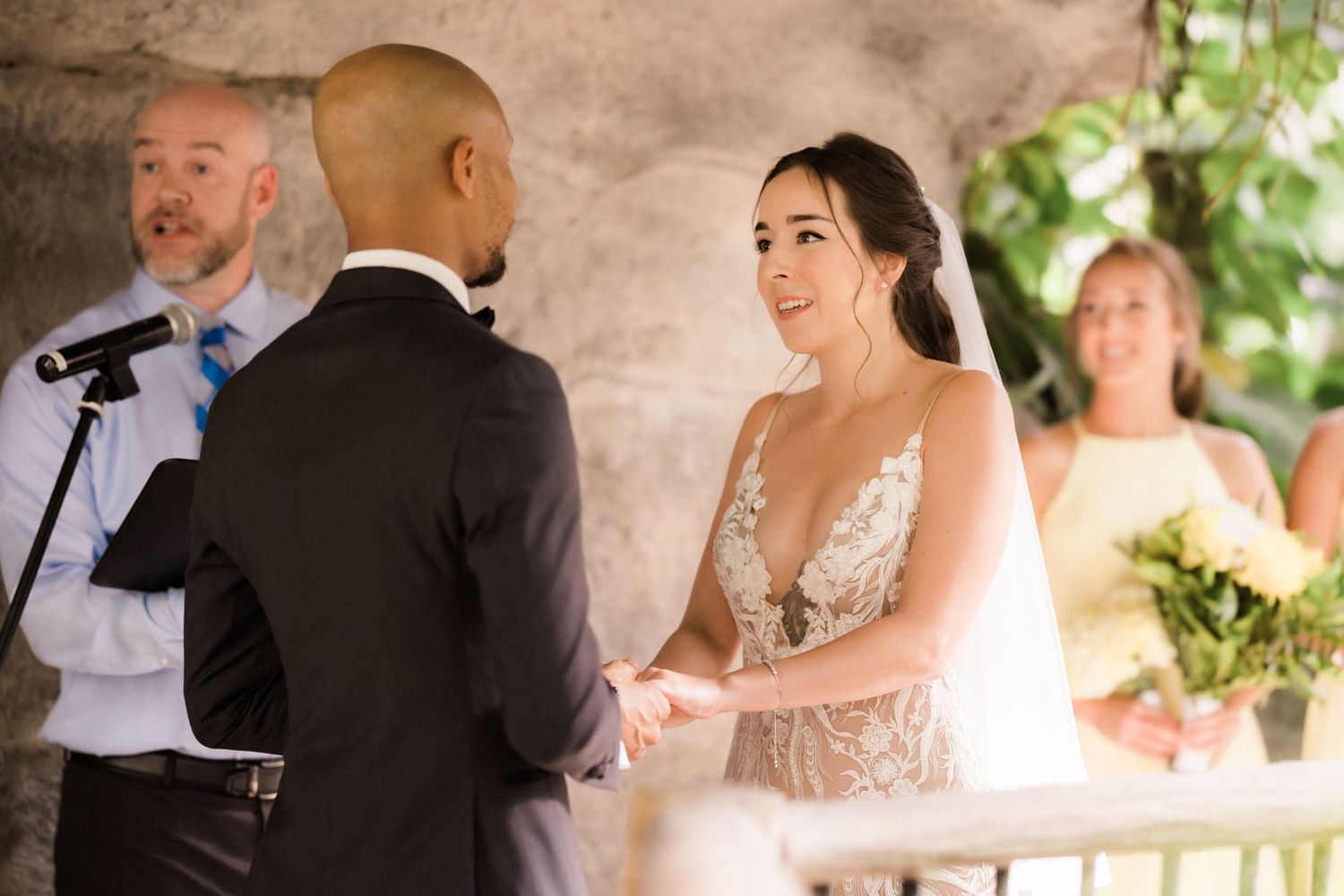 Sunlit wedding ceremony on stone terrace with floral decorations and officiant.