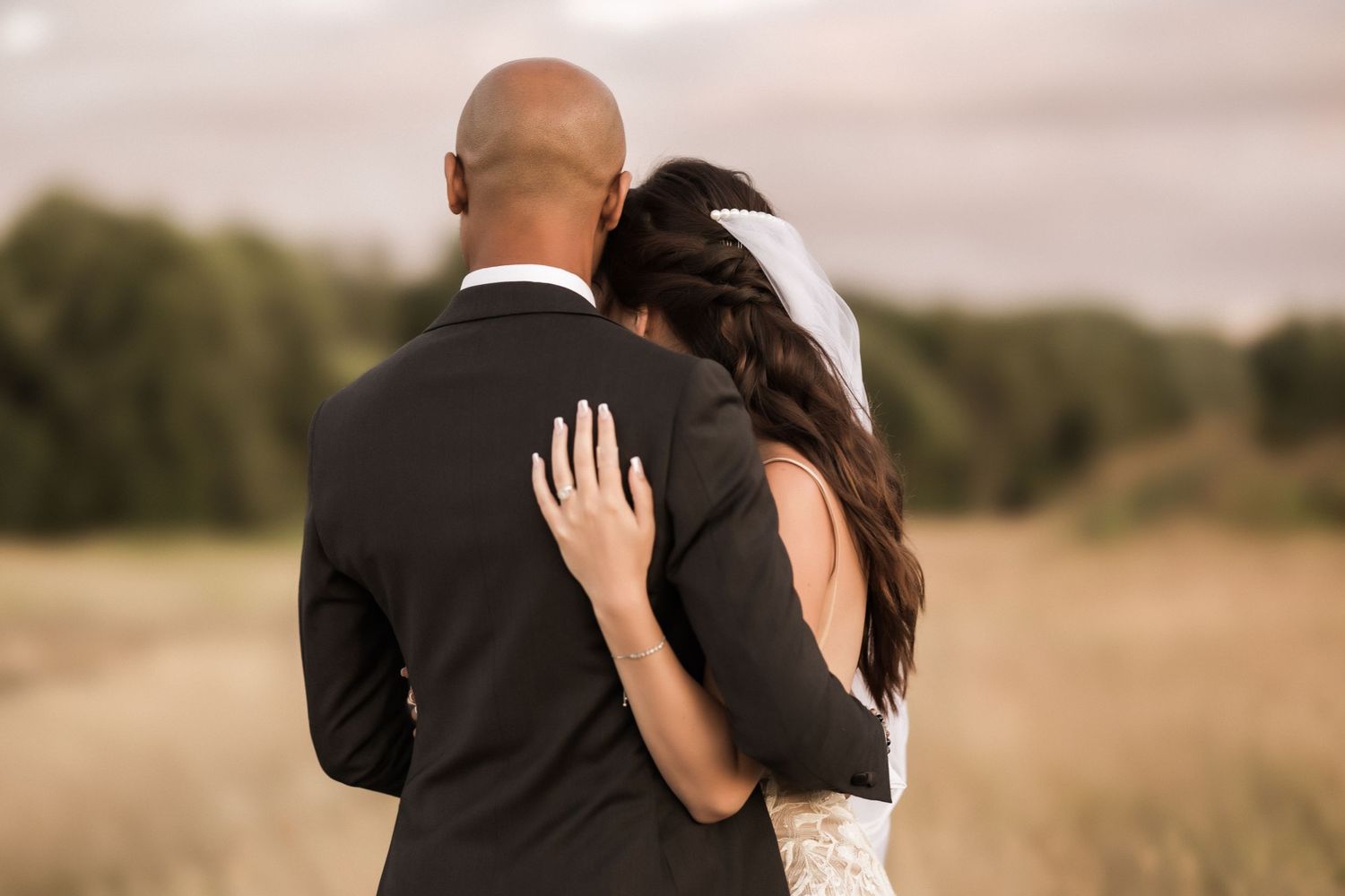 Rear view of newlyweds embracing while standing in a golden field at sunset.