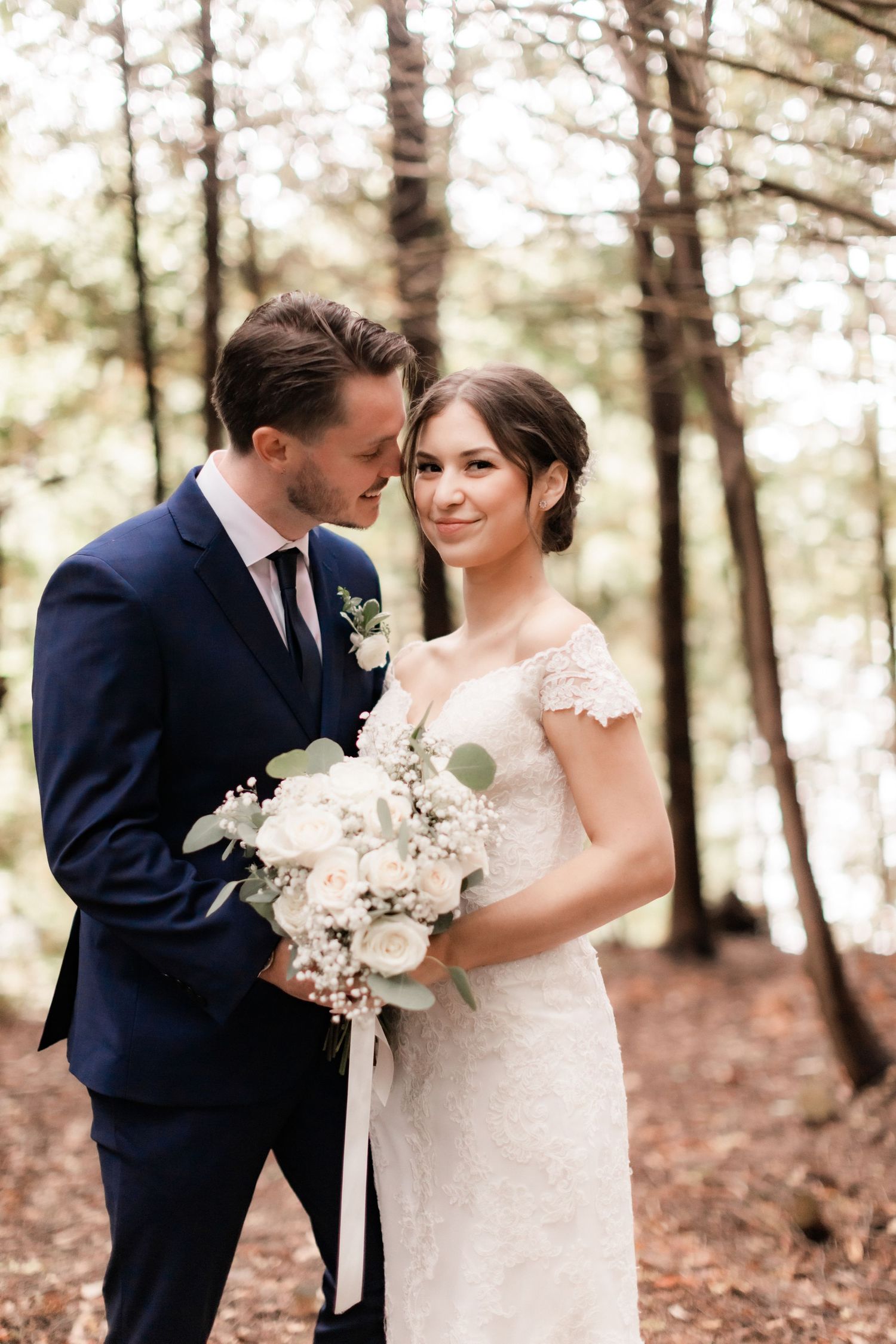 Wedding couple with white bouquet posing in woodlands with soft natural light.