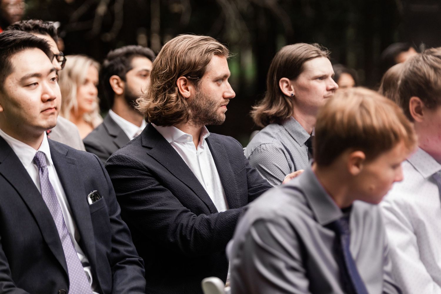 Wedding guests seated in formal attire during an outdoor ceremony.
