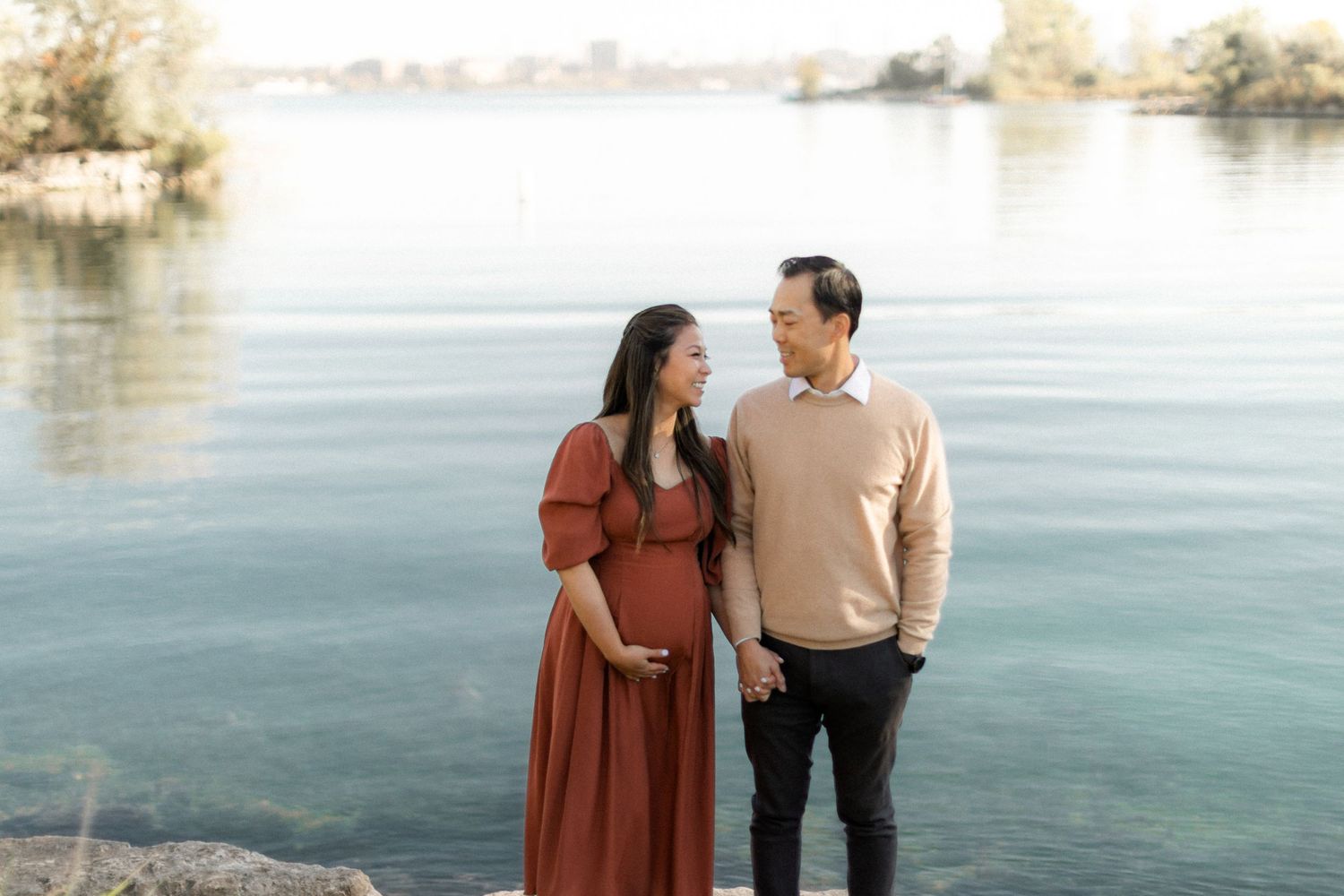 Couple in autumn attire share tender moment by peaceful waterfront.