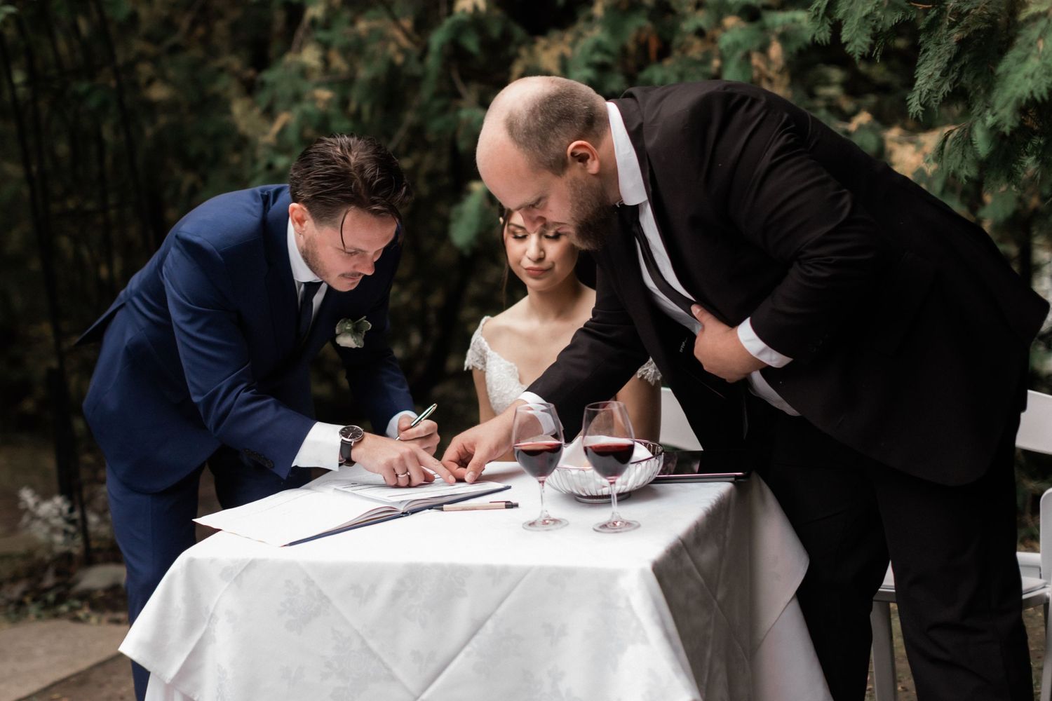 Wedding guests gather around a white-clothed table to sign official documents.