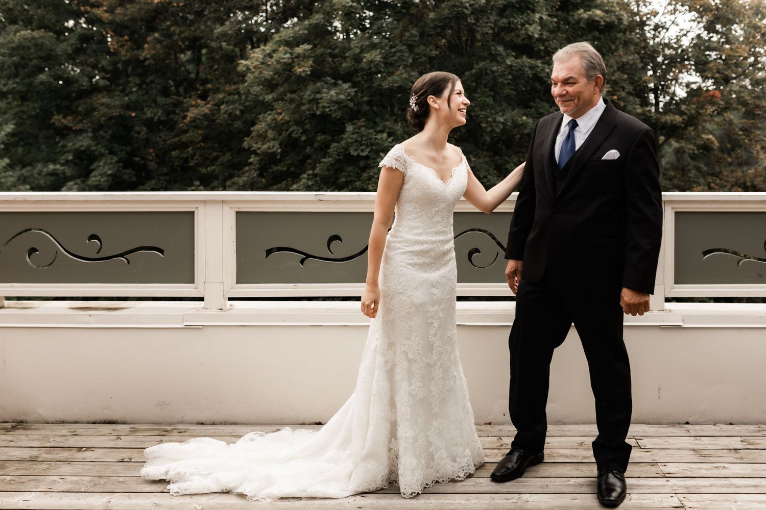 Bride and father share candid moment on wooden deck during wedding ceremony.