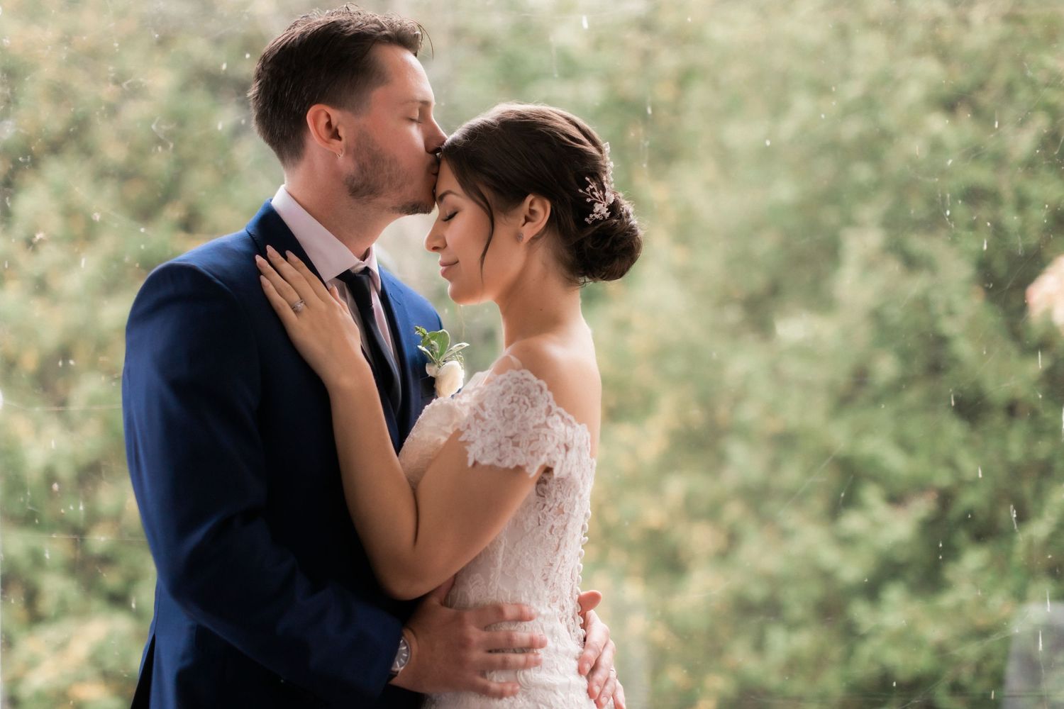 Intimate wedding portrait of couple embracing in formal attire against natural backdrop.