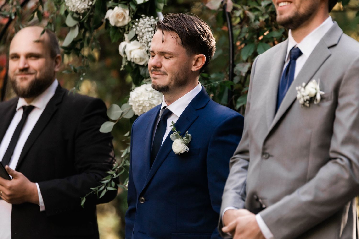 Groomsmen in formal attire stand together during an outdoor garden wedding ceremony.