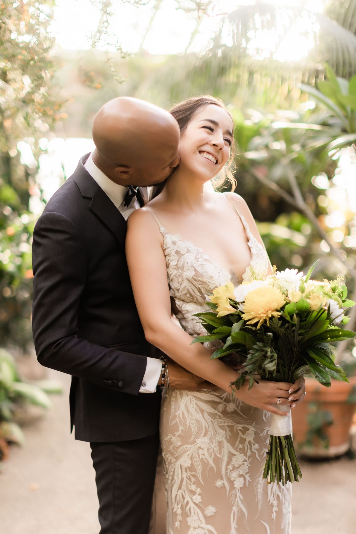 A tender wedding moment captured in a greenhouse with yellow flower bouquet.